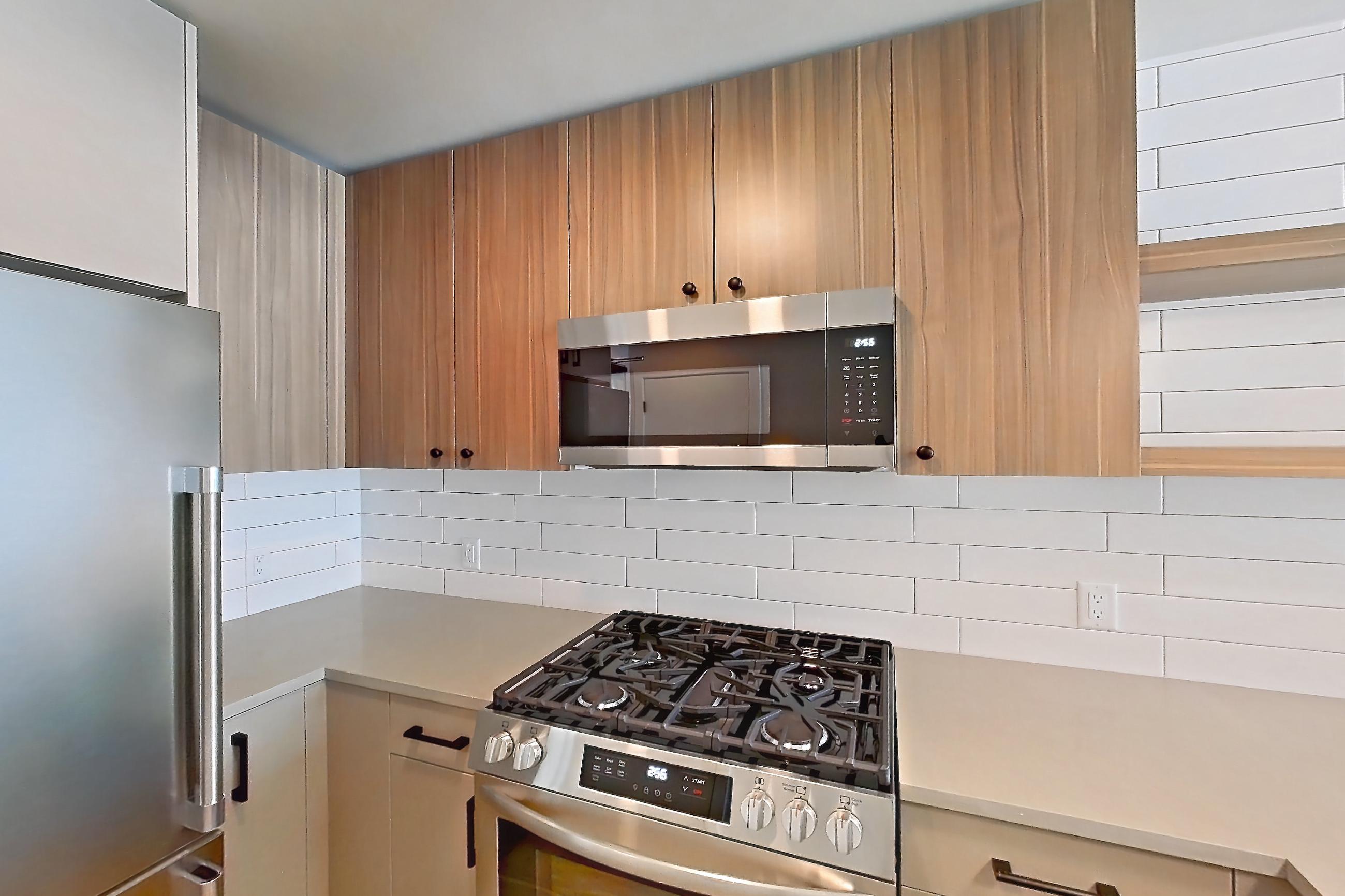 Kitchen with dishwasher, gas range, light countertops, light wood-finish flooring, microwave, oven/range, refrigerator, and stainless steel appliances, Apartment 614 at The Myles