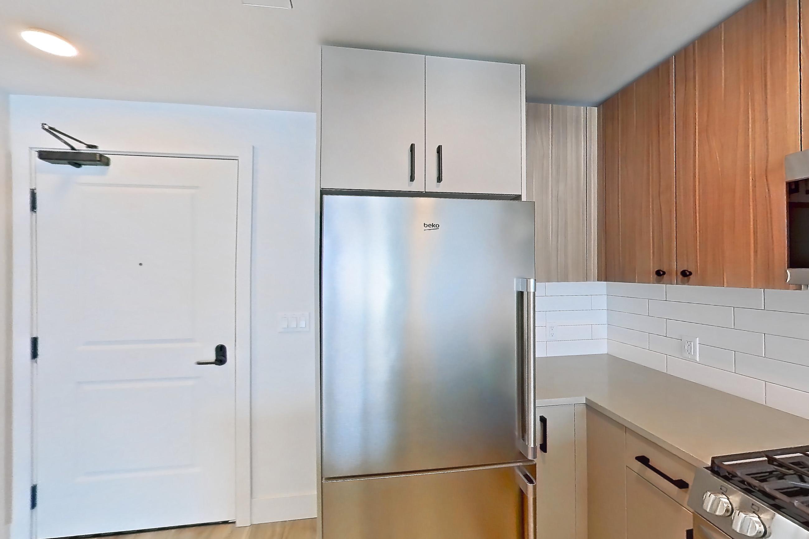 Kitchen with dishwasher, gas range, light countertops, light wood-finish flooring, microwave, oven/range, refrigerator, and stainless steel appliances, Apartment 614 at The Myles