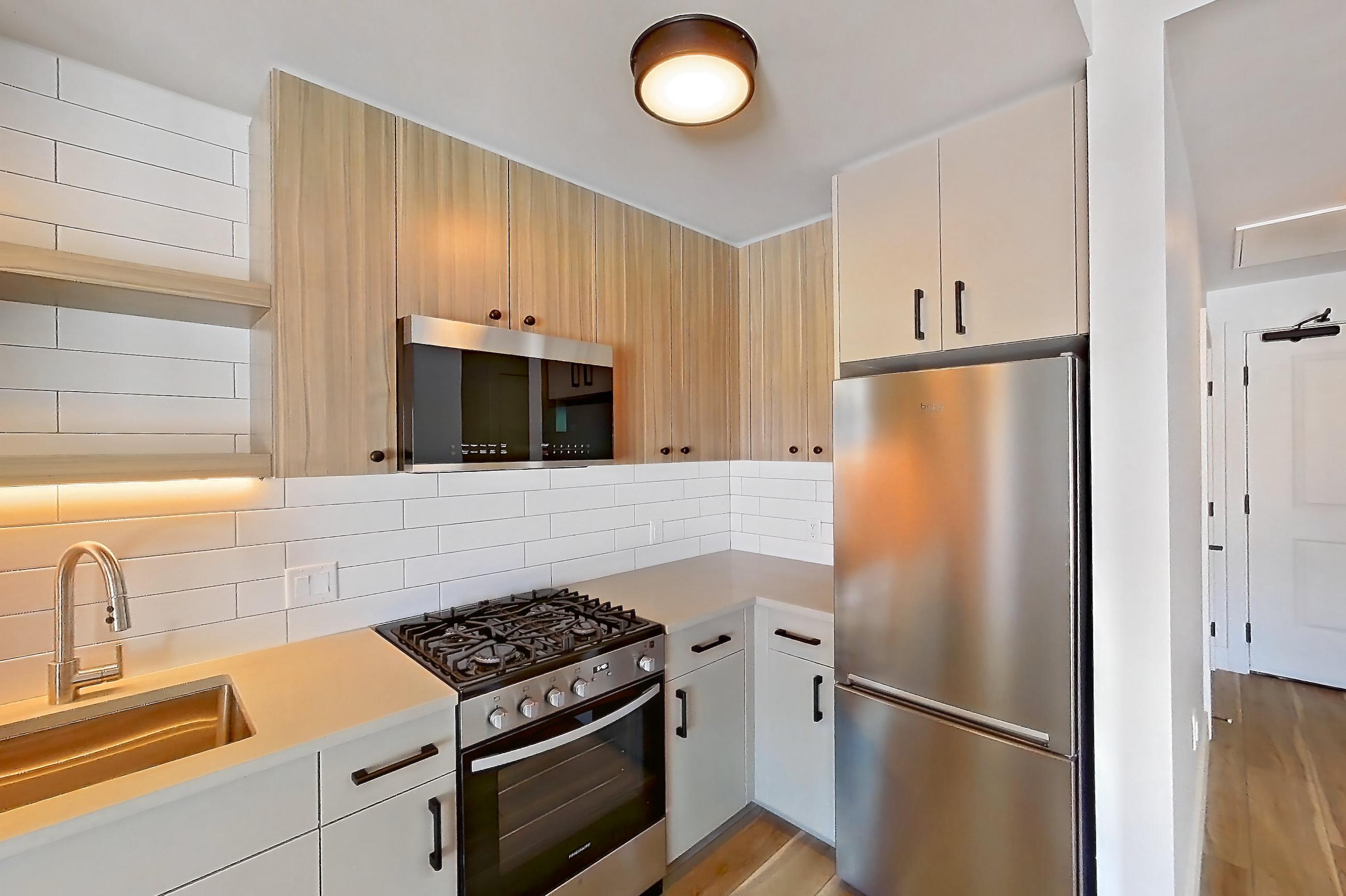 Kitchen with dishwasher, gas range, light countertops, light wood-finish flooring, oven/range, refrigerator, and stainless steel appliances, Apartment 620 at The Myles