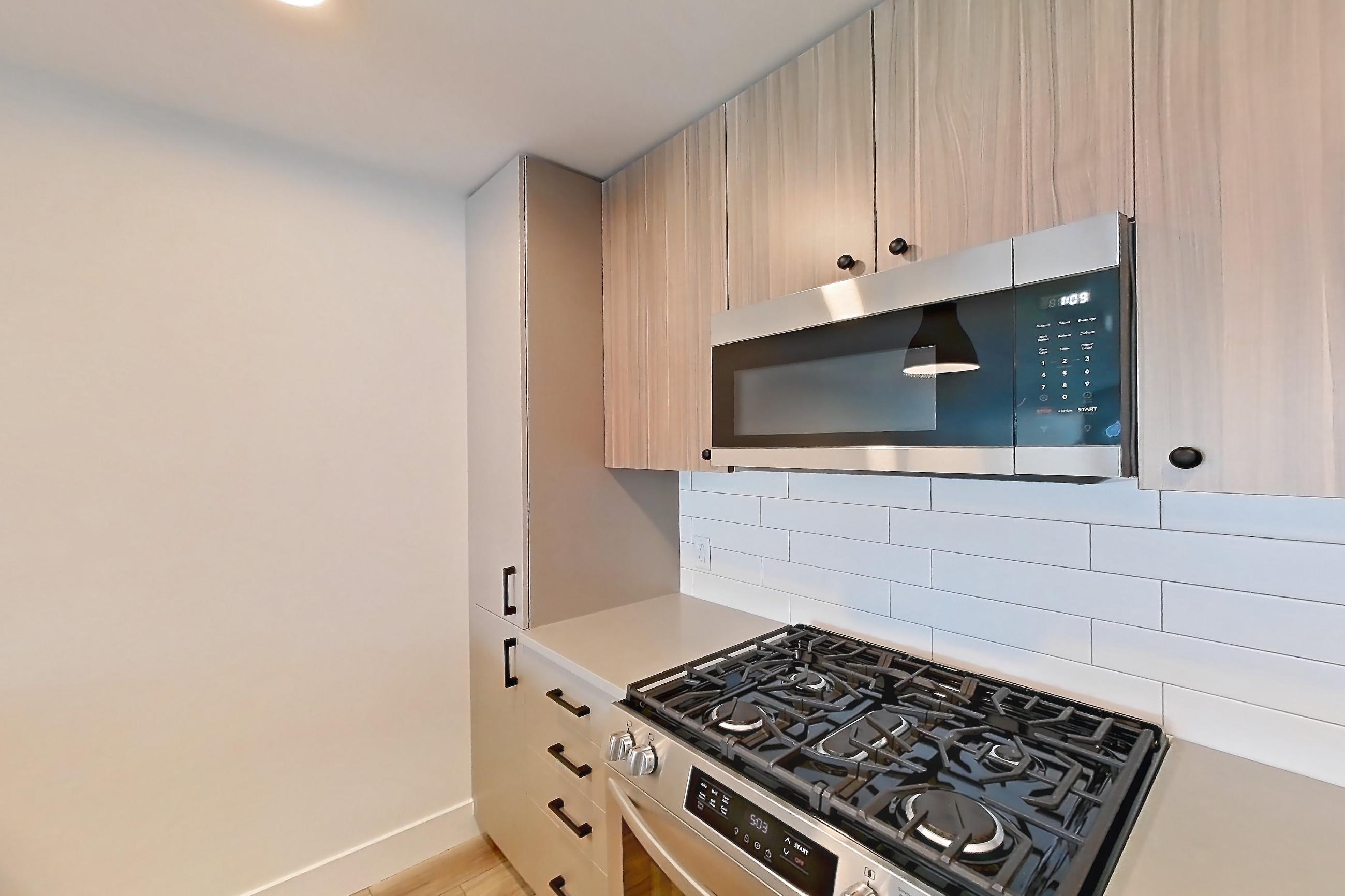 Kitchen with dishwasher, gas range, light countertops, light wood-finish flooring, microwave, oven/range, refrigerator, and stainless steel appliances, Apartment 621 at The Myles