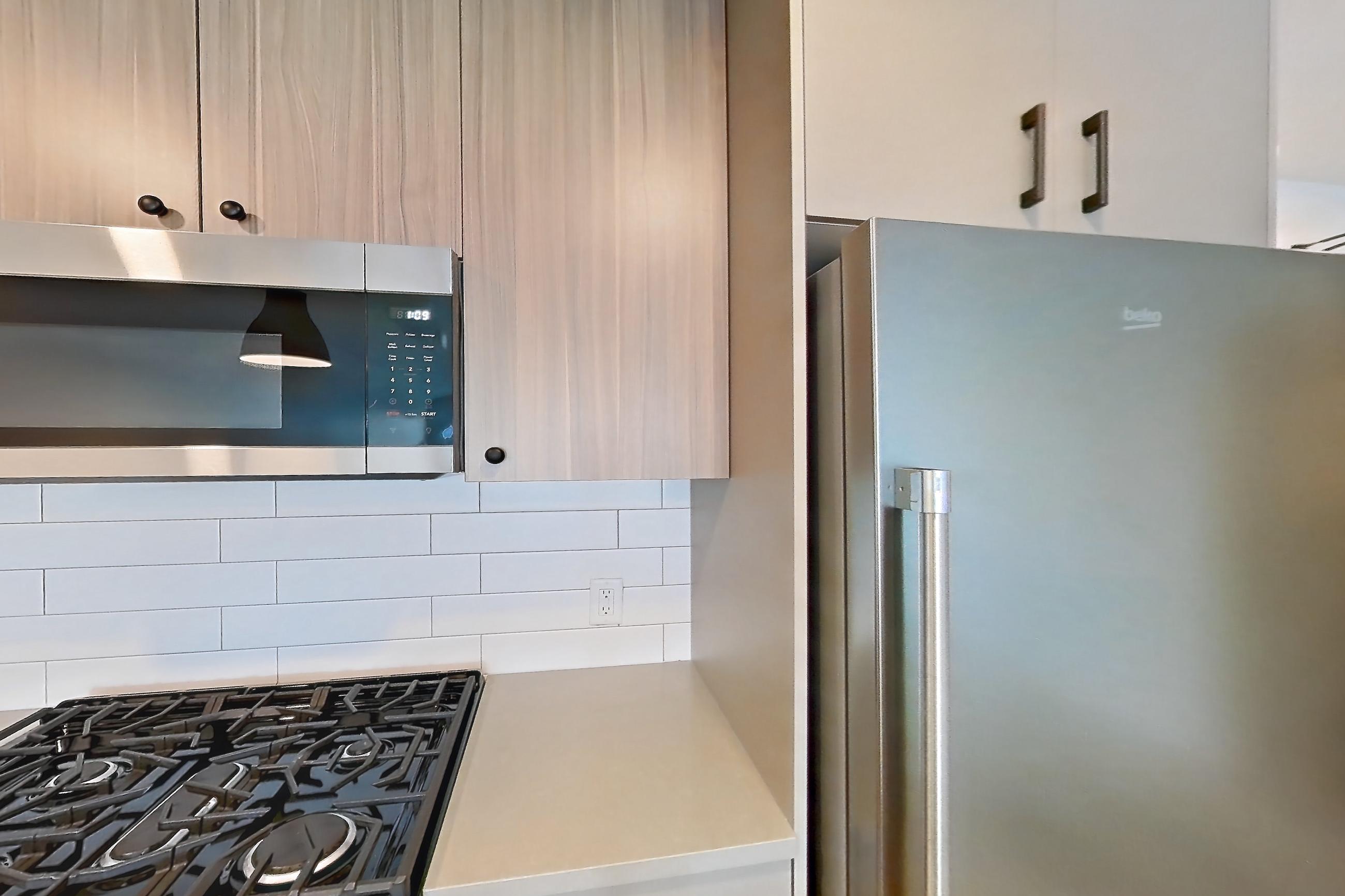 Kitchen with dishwasher, gas range, light countertops, light wood-finish flooring, microwave, oven/range, refrigerator, and stainless steel appliances, Apartment 621 at The Myles