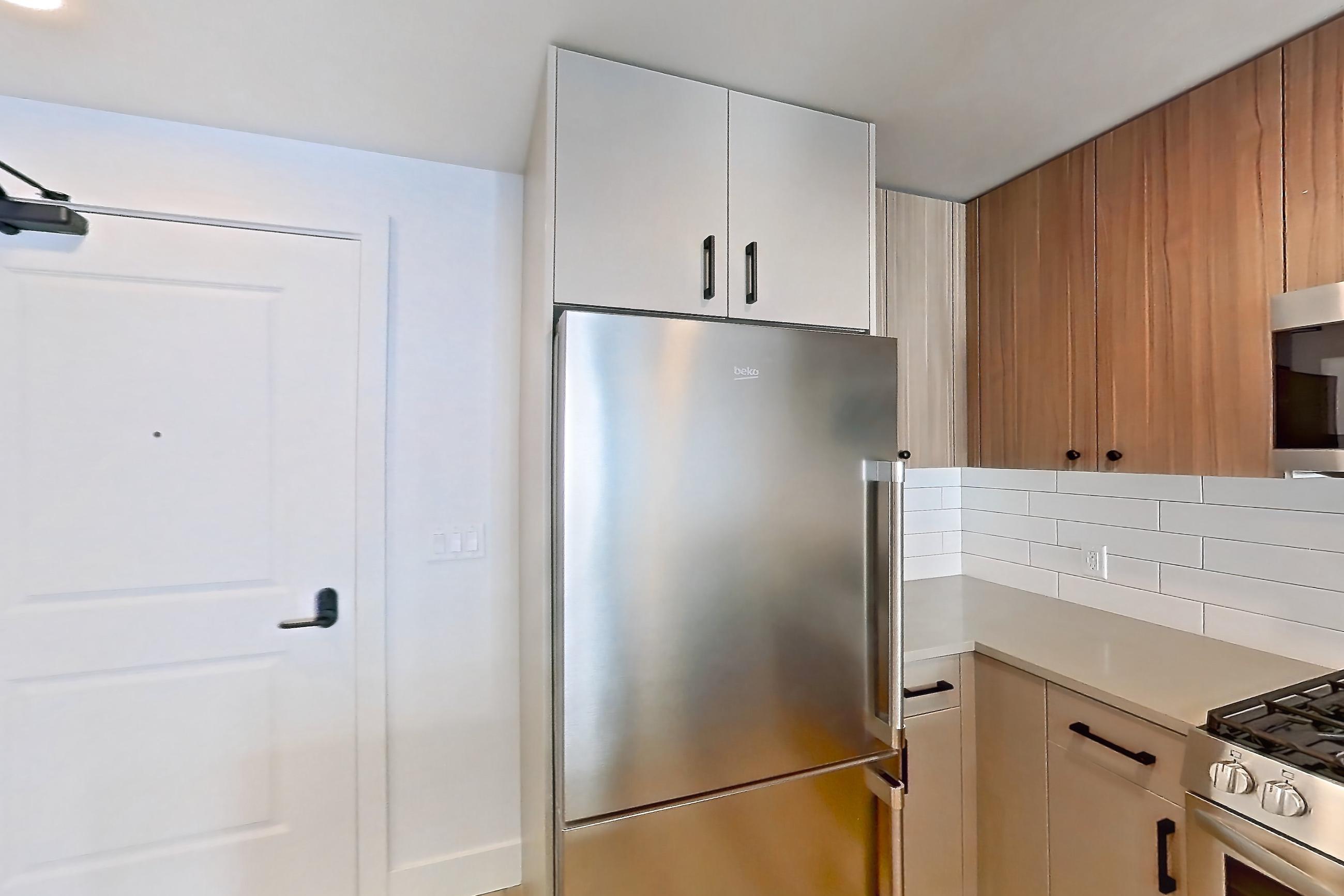 Kitchen with dishwasher, gas range, kitchen island, light countertops, light wood-finish flooring, microwave, oven/range, refrigerator, and stainless steel appliances, Apartment 627 at The Myles