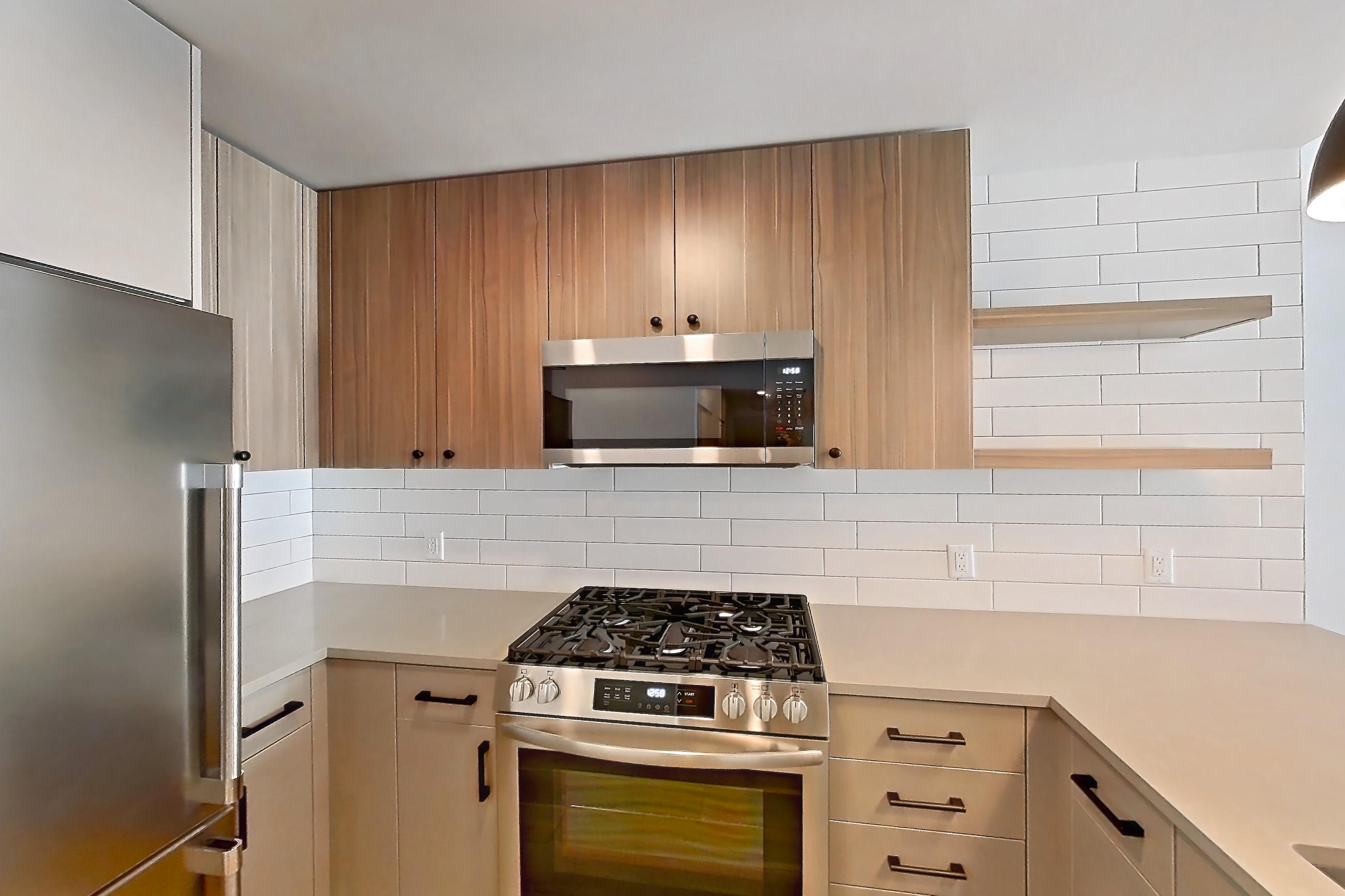 Kitchen with dishwasher, gas range, kitchen island, light countertops, light wood-finish flooring, microwave, oven/range, refrigerator, and stainless steel appliances, Apartment 627 at The Myles