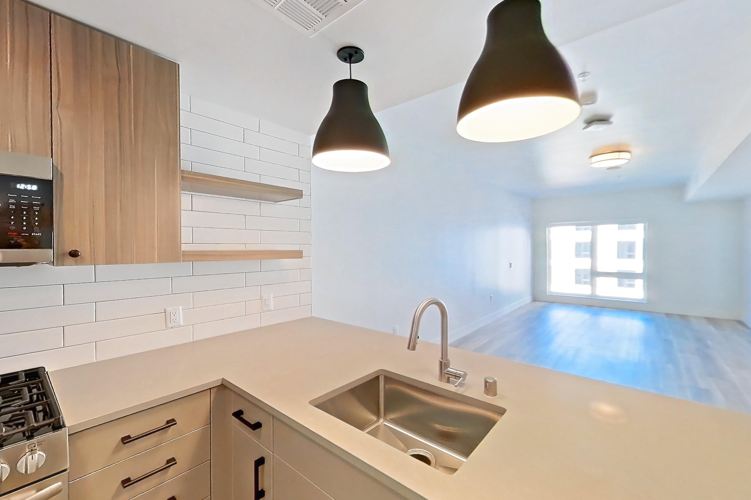 Kitchen with dishwasher, gas range, kitchen island, light countertops, light wood-finish flooring, microwave, oven/range, refrigerator, and stainless steel appliances, Apartment 627 at The Myles