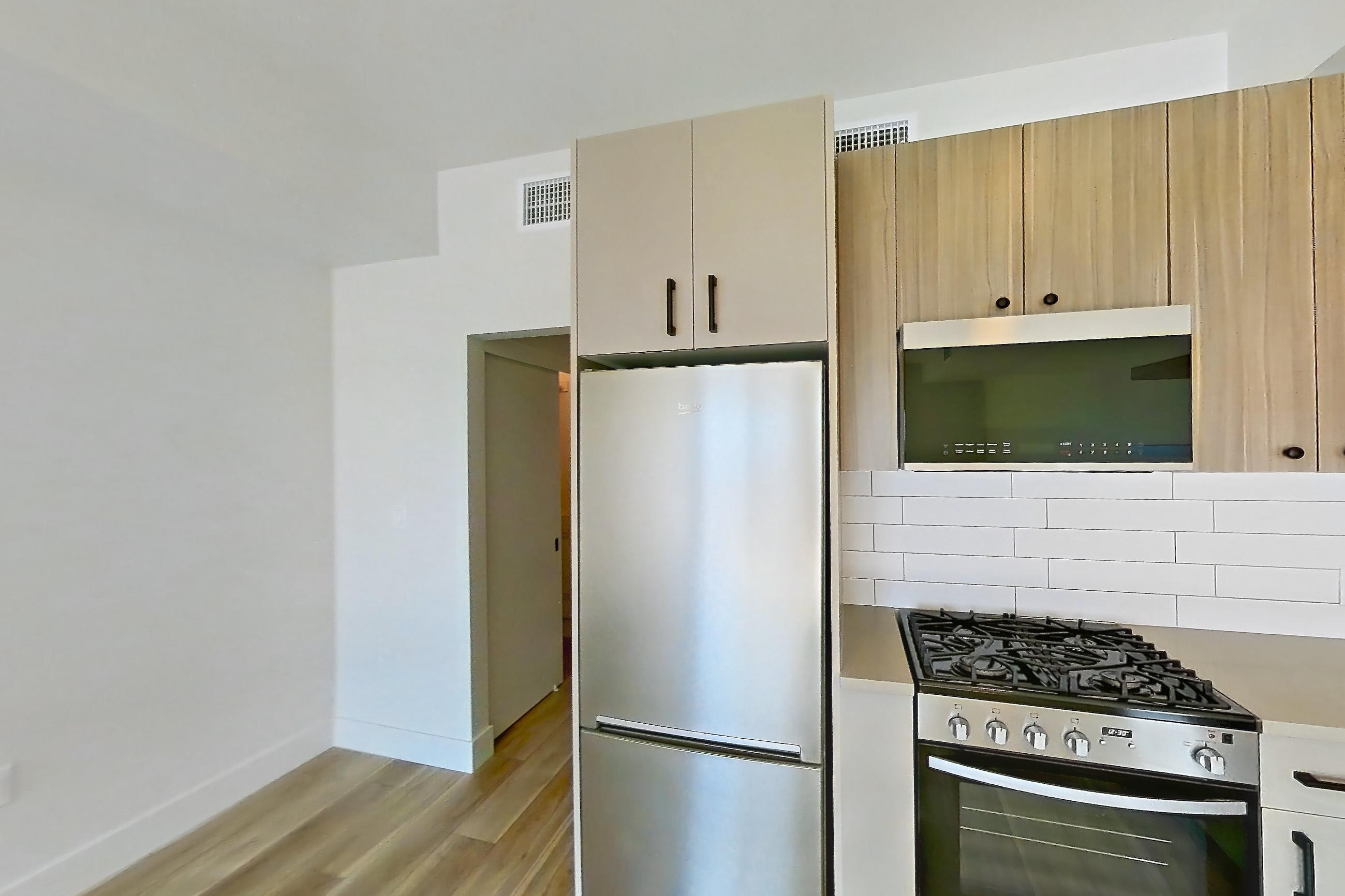 Kitchen with dishwasher, gas range, light countertops, light wood-finish flooring, oven/range, and stainless steel appliances, Apartment 628 at The Myles