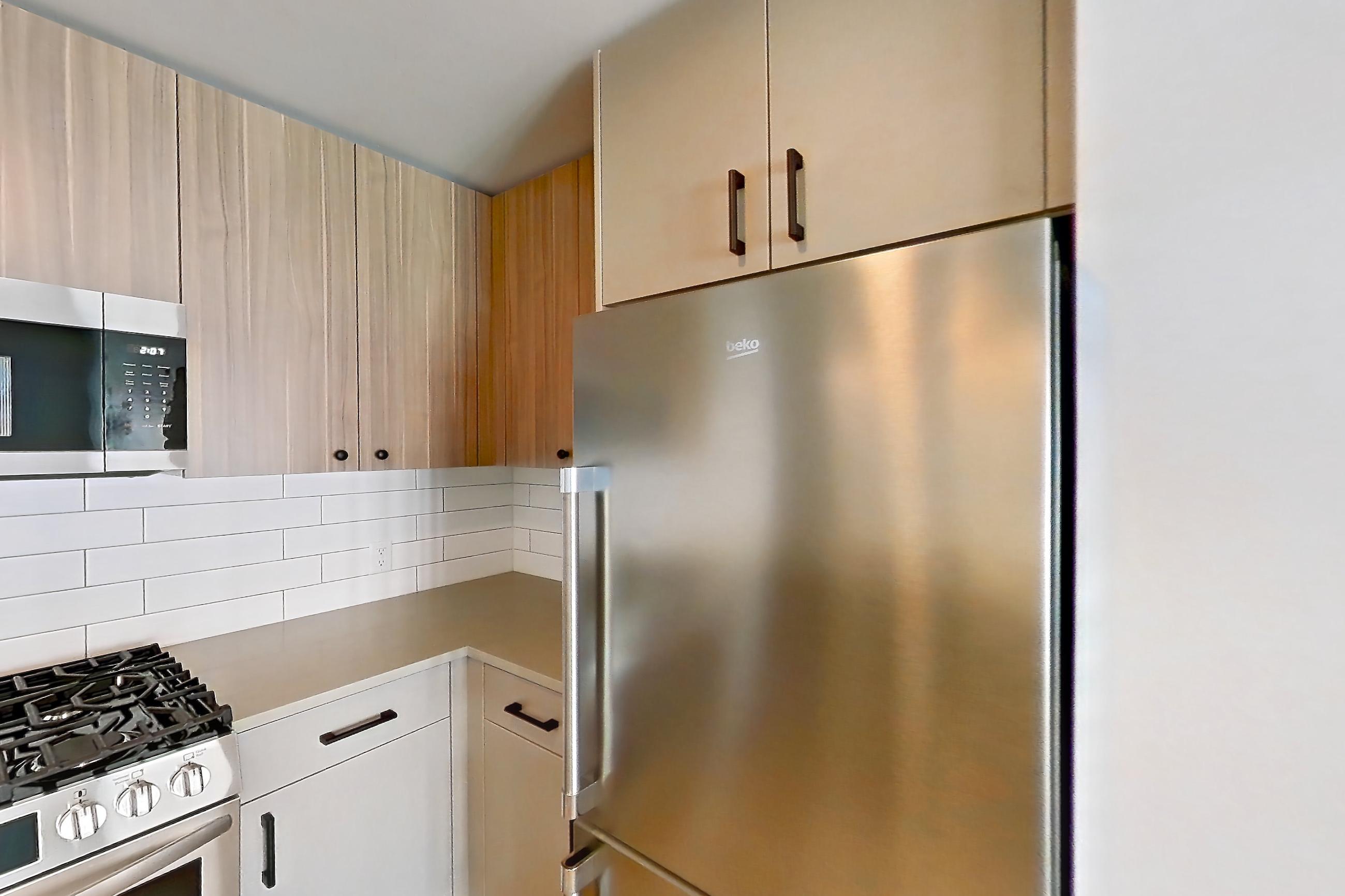 Kitchen with dishwasher, gas range, light countertops, light wood-finish flooring, microwave, oven/range, refrigerator, stainless steel appliances, and white appliances, Apartment 629 at The Myles