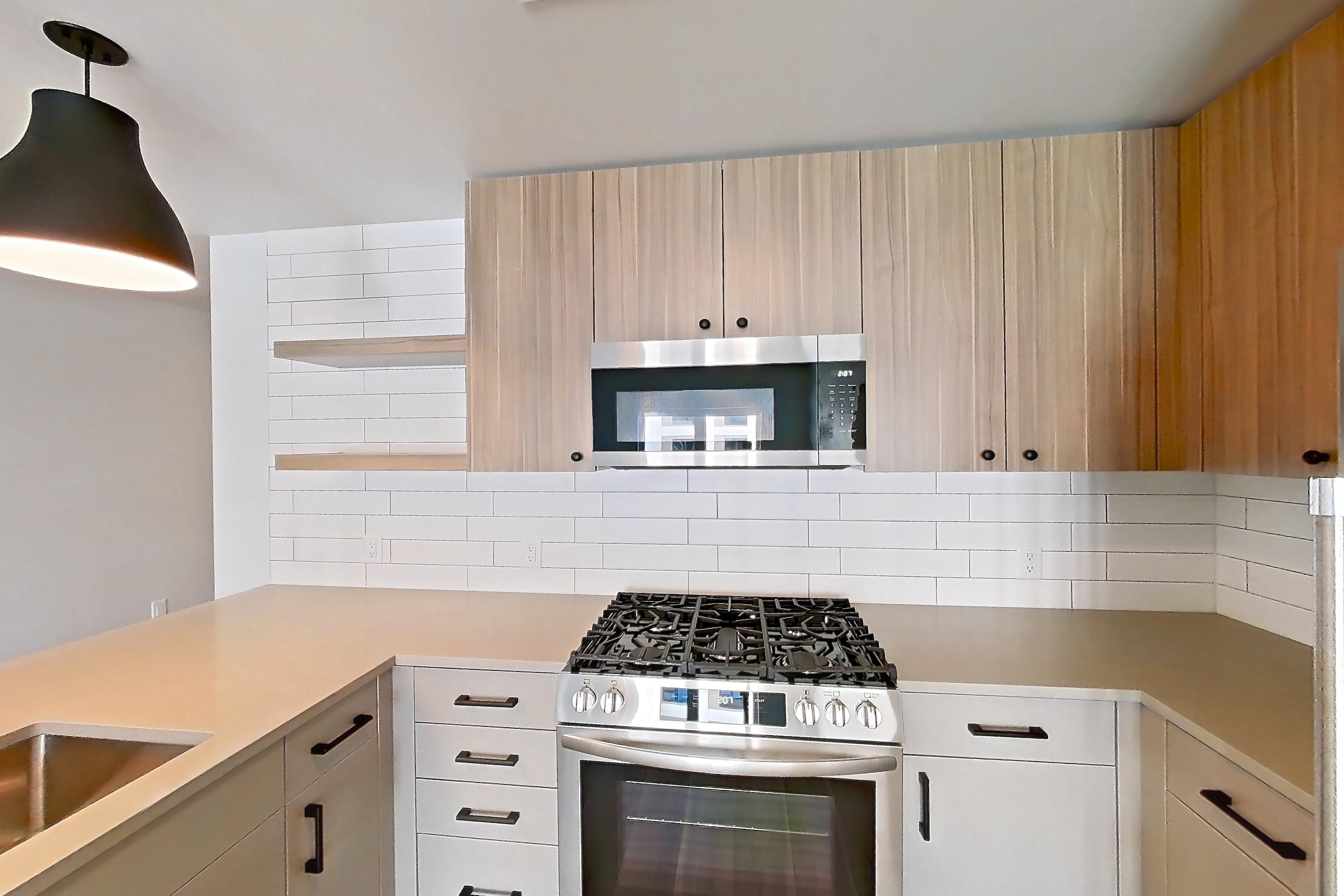 Kitchen with dishwasher, gas range, light countertops, light wood-finish flooring, microwave, oven/range, refrigerator, stainless steel appliances, and white appliances, Apartment 629 at The Myles