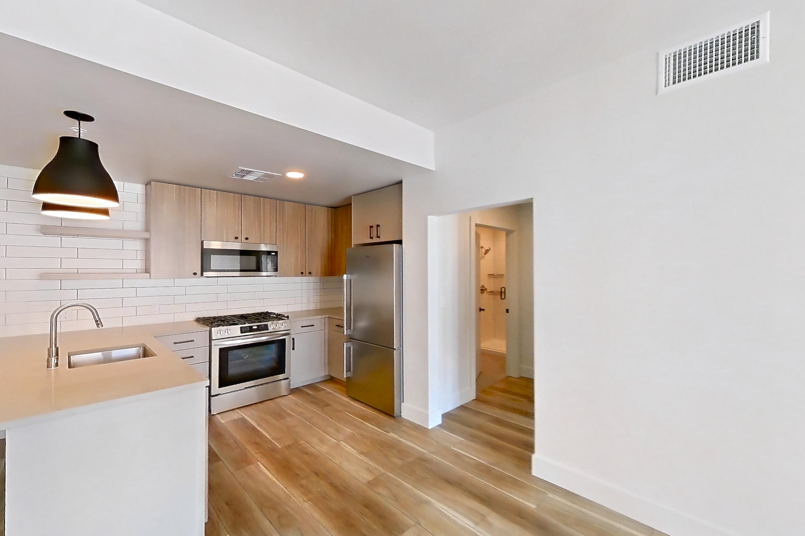 Living room with light countertops, light wood-finish flooring, oven/range, refrigerator, stainless steel appliances, and white appliances, Apartment 629 at The Myles