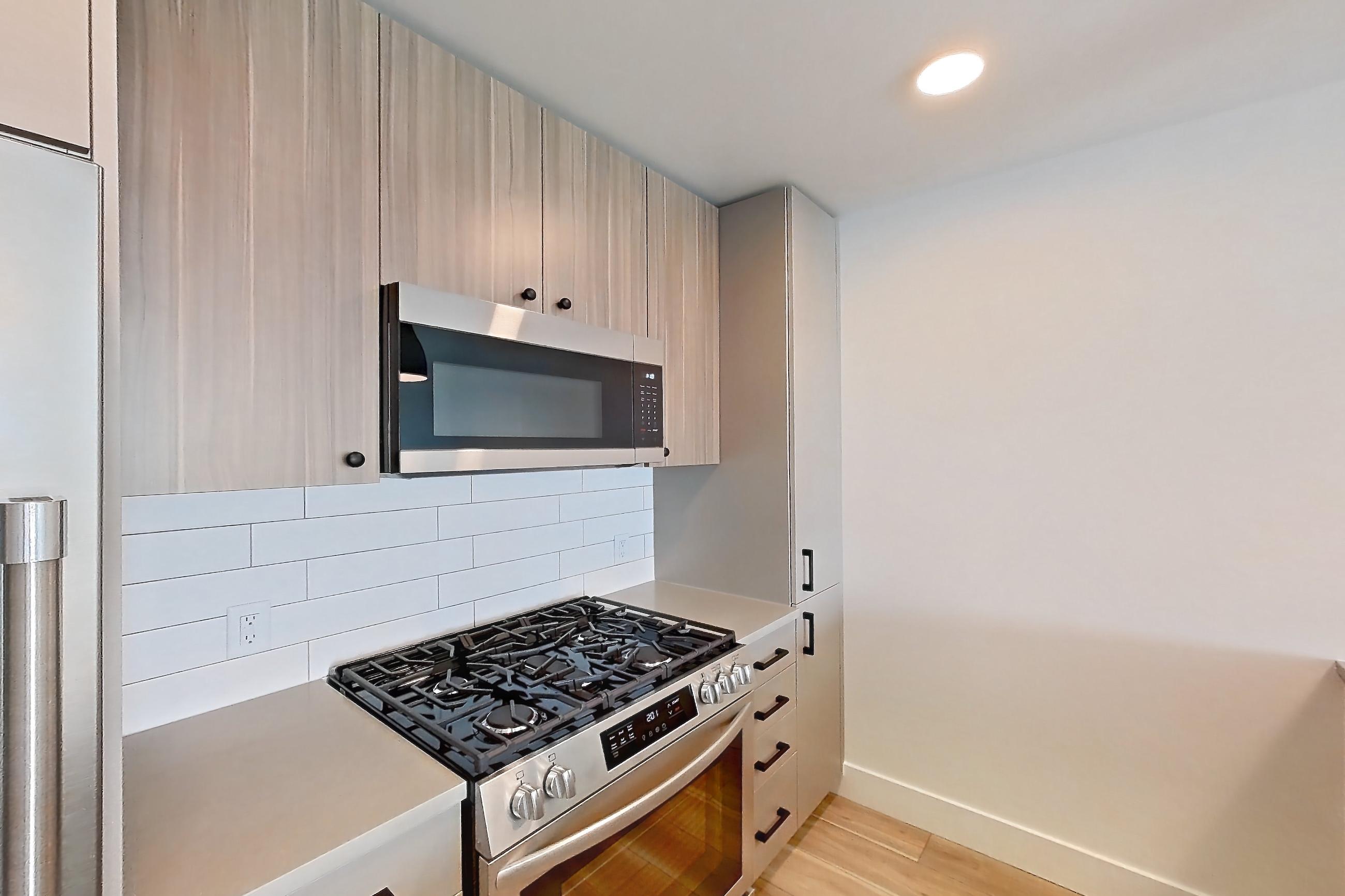 Kitchen with dishwasher, gas range, light countertops, light wood-finish flooring, microwave, oven/range, and stainless steel appliances, Apartment 630 at The Myles