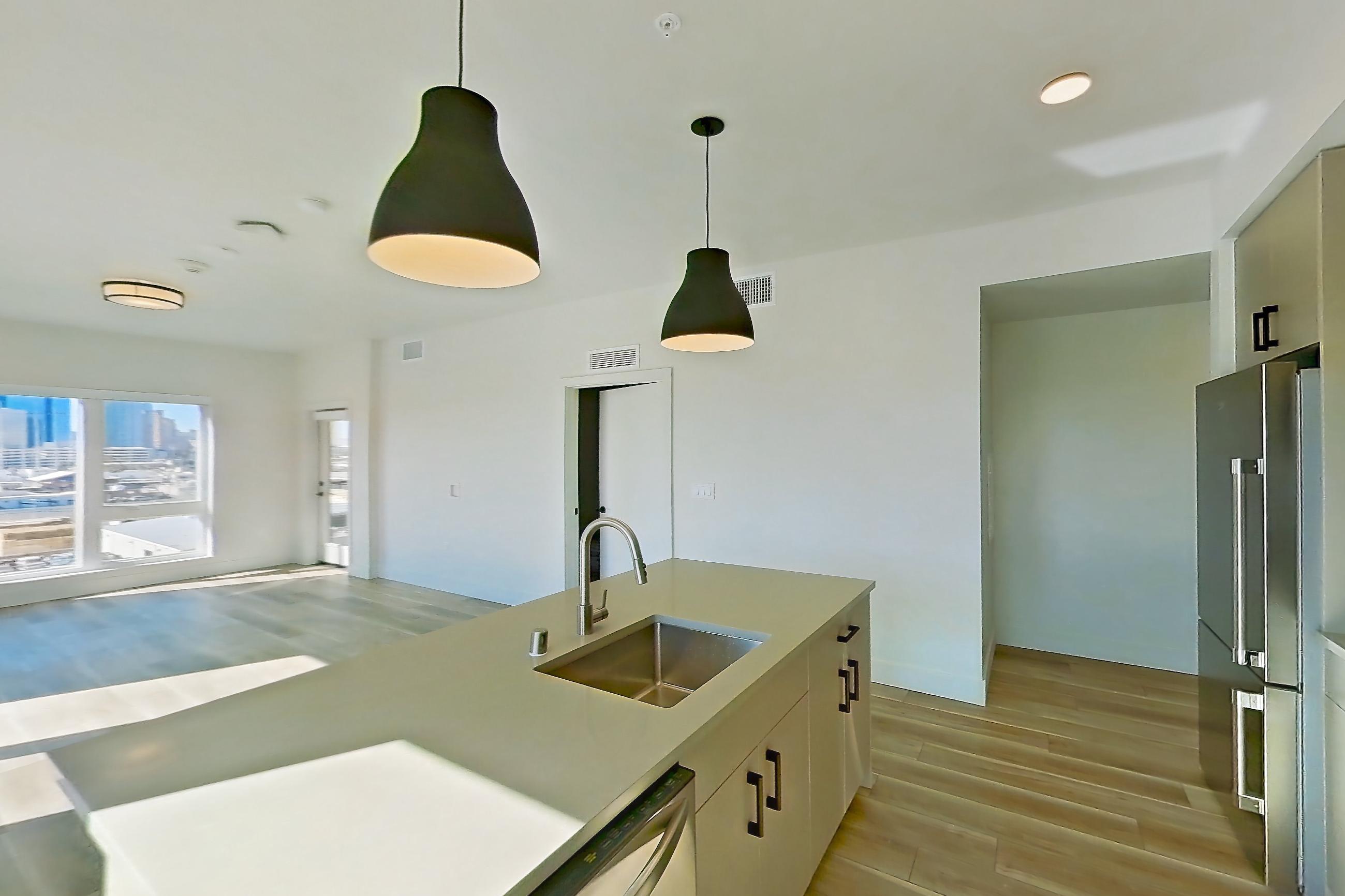 Kitchen with dishwasher, gas range, kitchen island, light countertops, light stone countertops, light wood-finish flooring, microwave, oven/range, refrigerator, stainless steel appliances, and wood-look tile flooring, Apartment 631 at The Myles