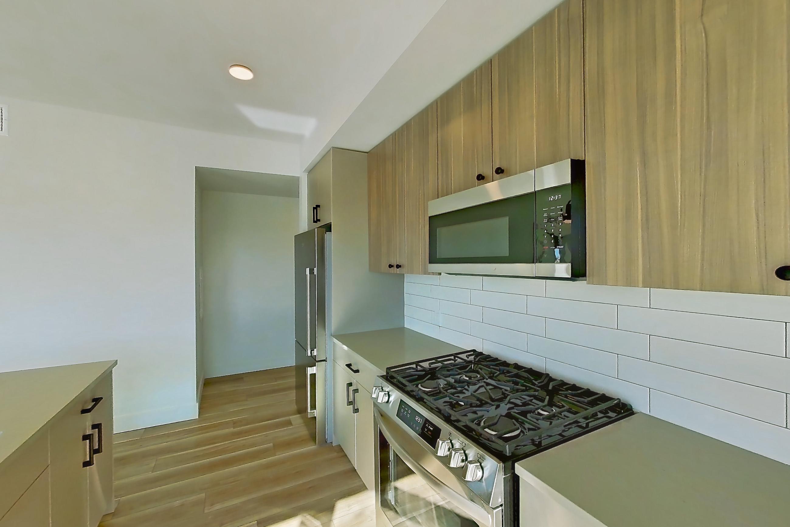 Kitchen with dishwasher, gas range, kitchen island, light countertops, light stone countertops, light wood-finish flooring, microwave, oven/range, refrigerator, stainless steel appliances, and wood-look tile flooring, Apartment 631 at The Myles