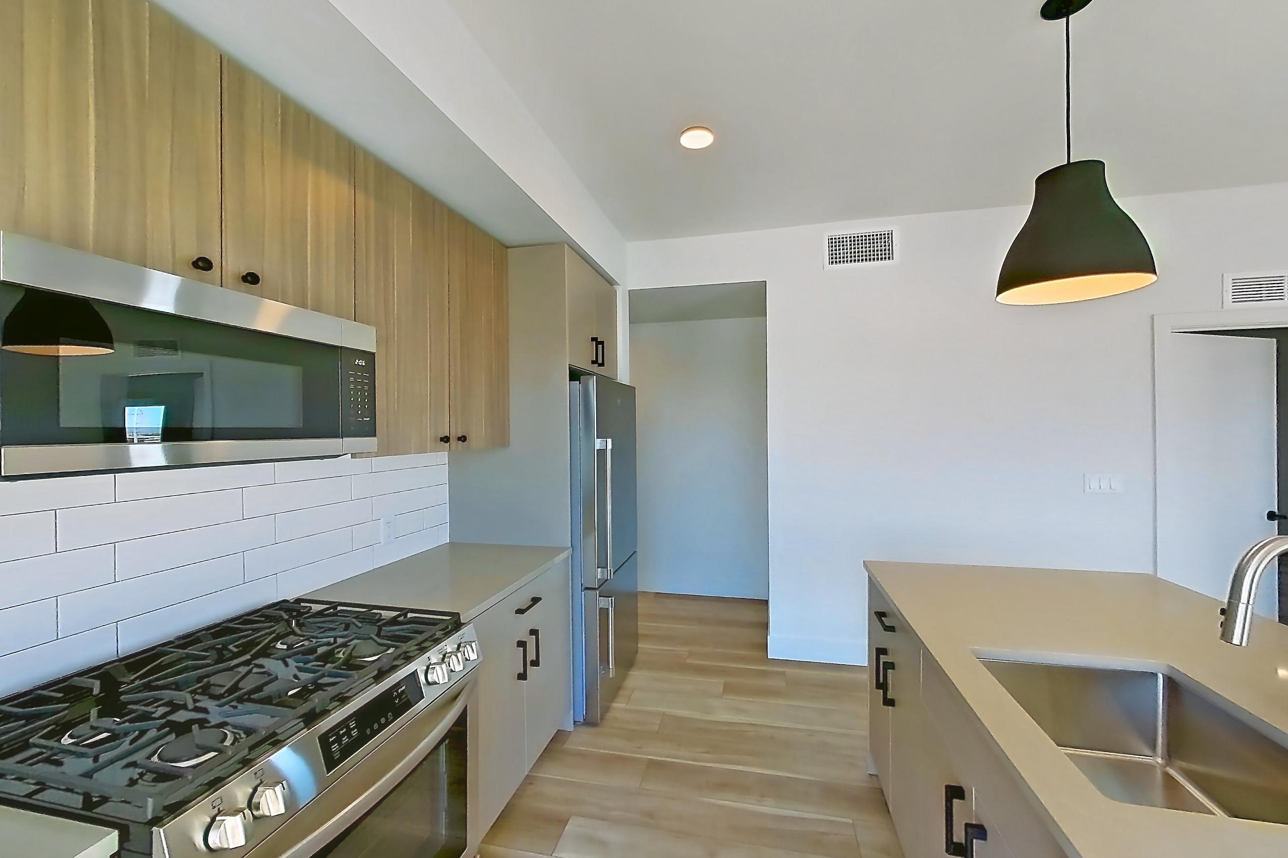 Kitchen with gas range, kitchen island, light countertops, light stone countertops, light wood-finish flooring, oven/range, refrigerator, and stainless steel appliances, Apartment 624 at The Myles