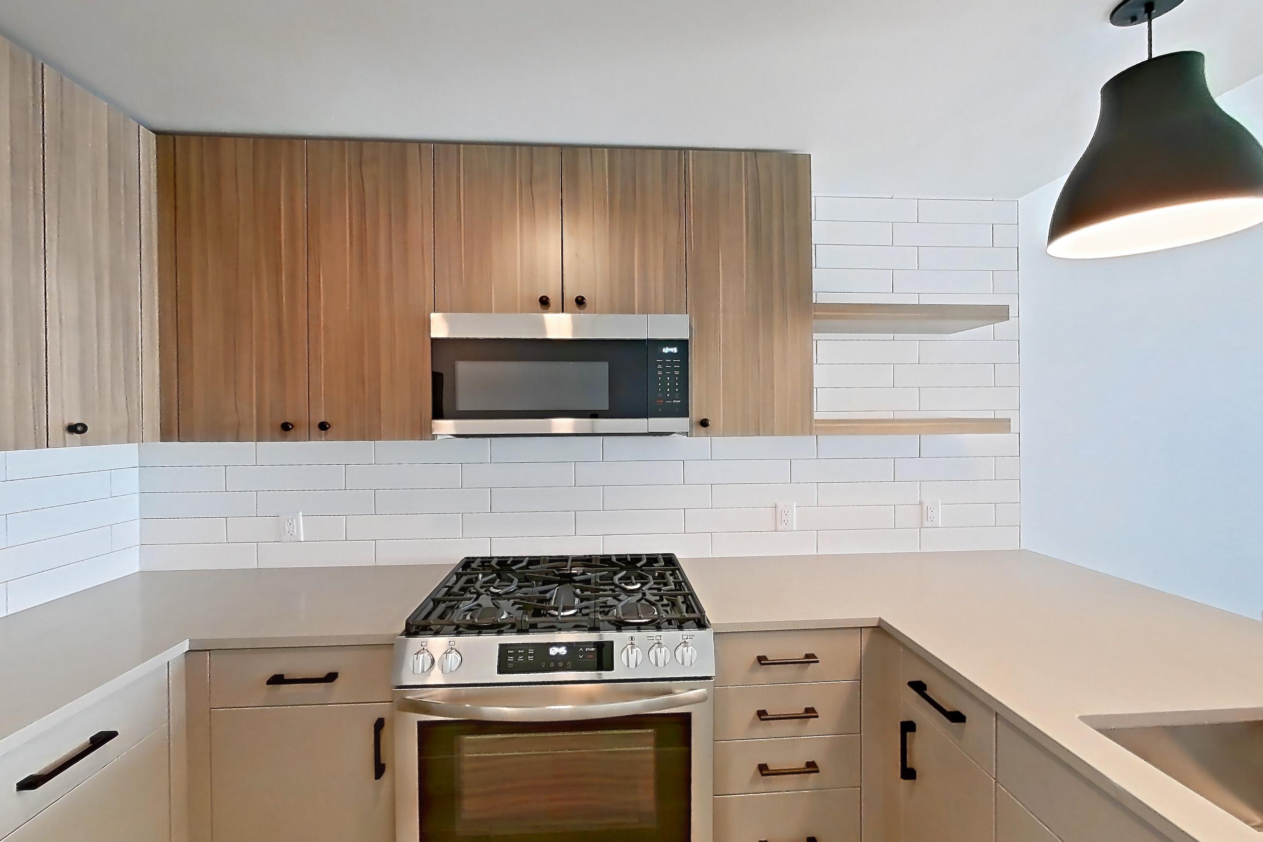 Kitchen with dishwasher, gas range, light countertops, light wood-finish flooring, oven/range, refrigerator, and stainless steel appliances, Apartment 625 at The Myles