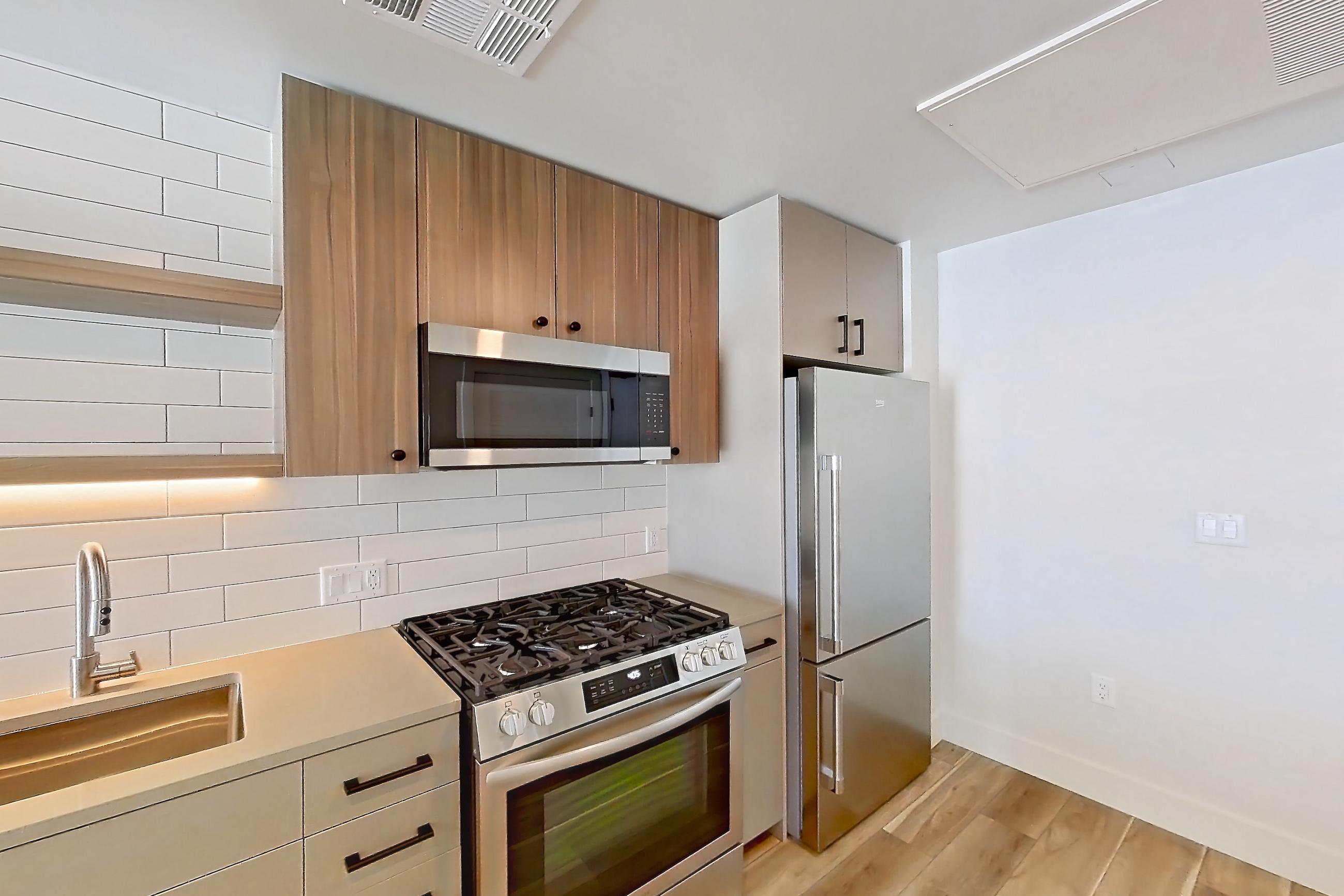 Kitchen with dishwasher, gas range, light countertops, light wood-finish flooring, microwave, oven/range, refrigerator, and stainless steel appliances, Apartment 634 at The Myles
