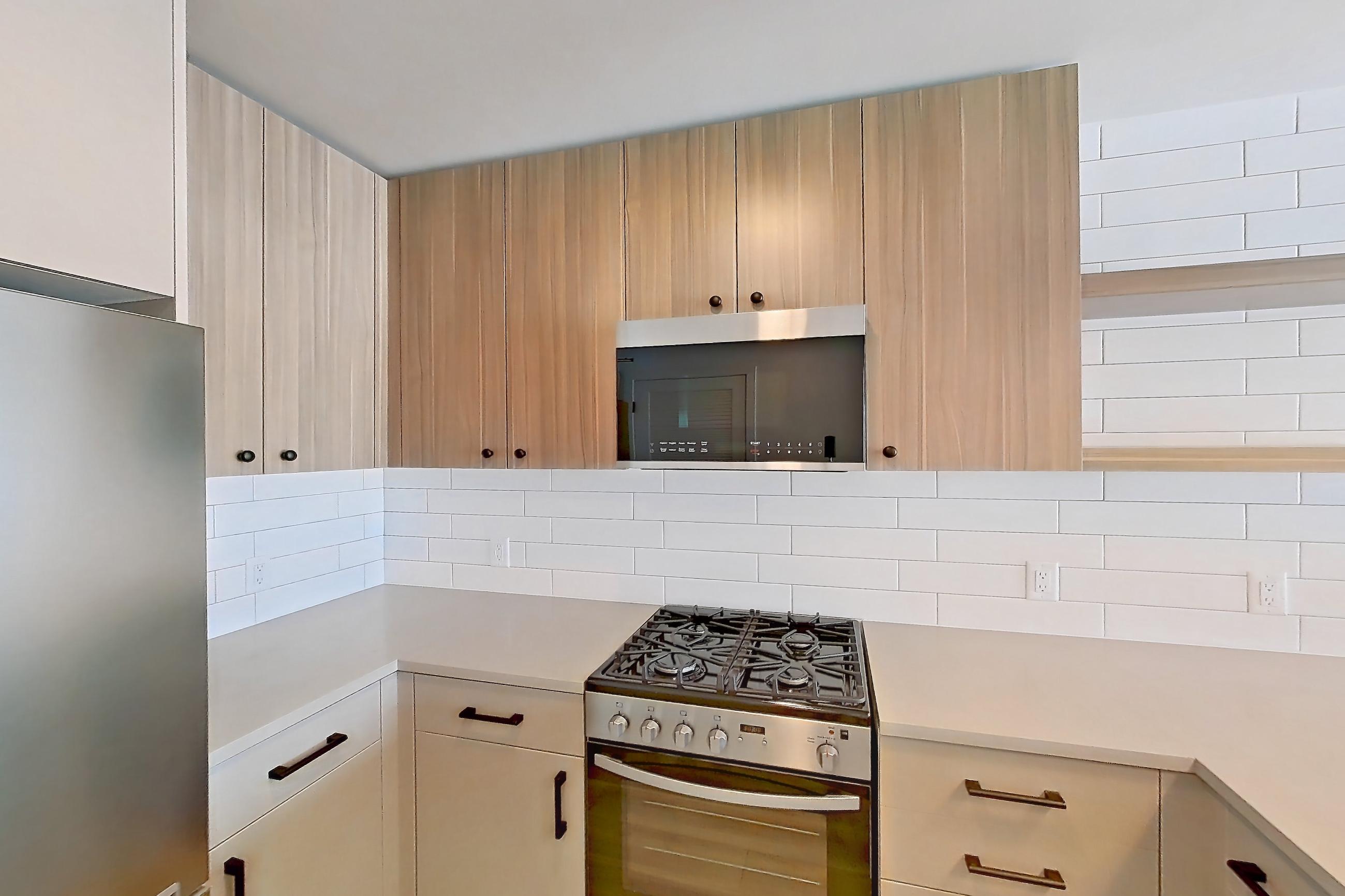 Kitchen with dishwasher, gas range, light countertops, light wood-finish flooring, oven/range, refrigerator, and stainless steel appliances, Apartment 635 at The Myles