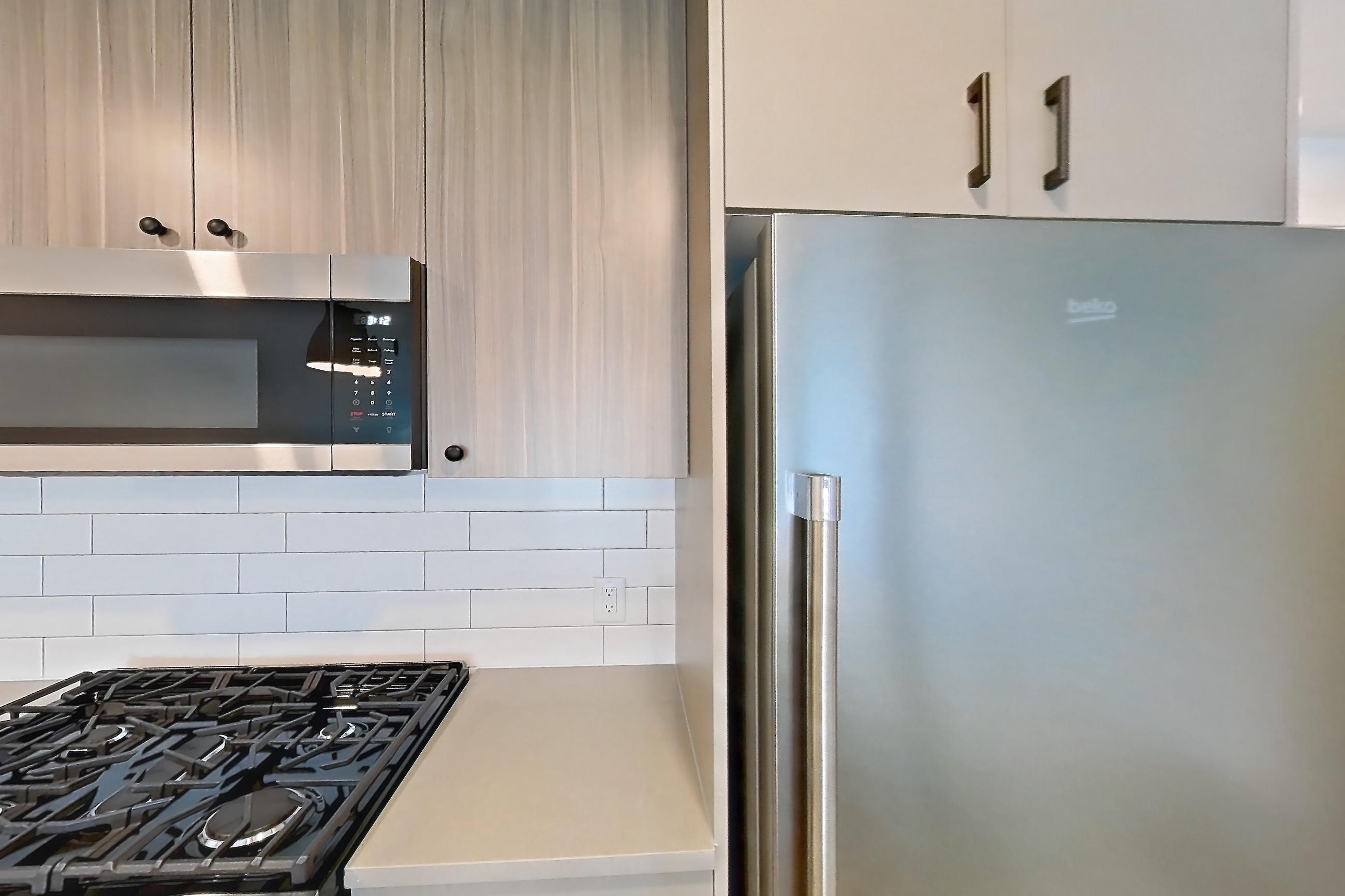 Kitchen with dishwasher, gas range, light countertops, light wood-finish flooring, oven/range, refrigerator, and stainless steel appliances, Apartment 636 at The Myles