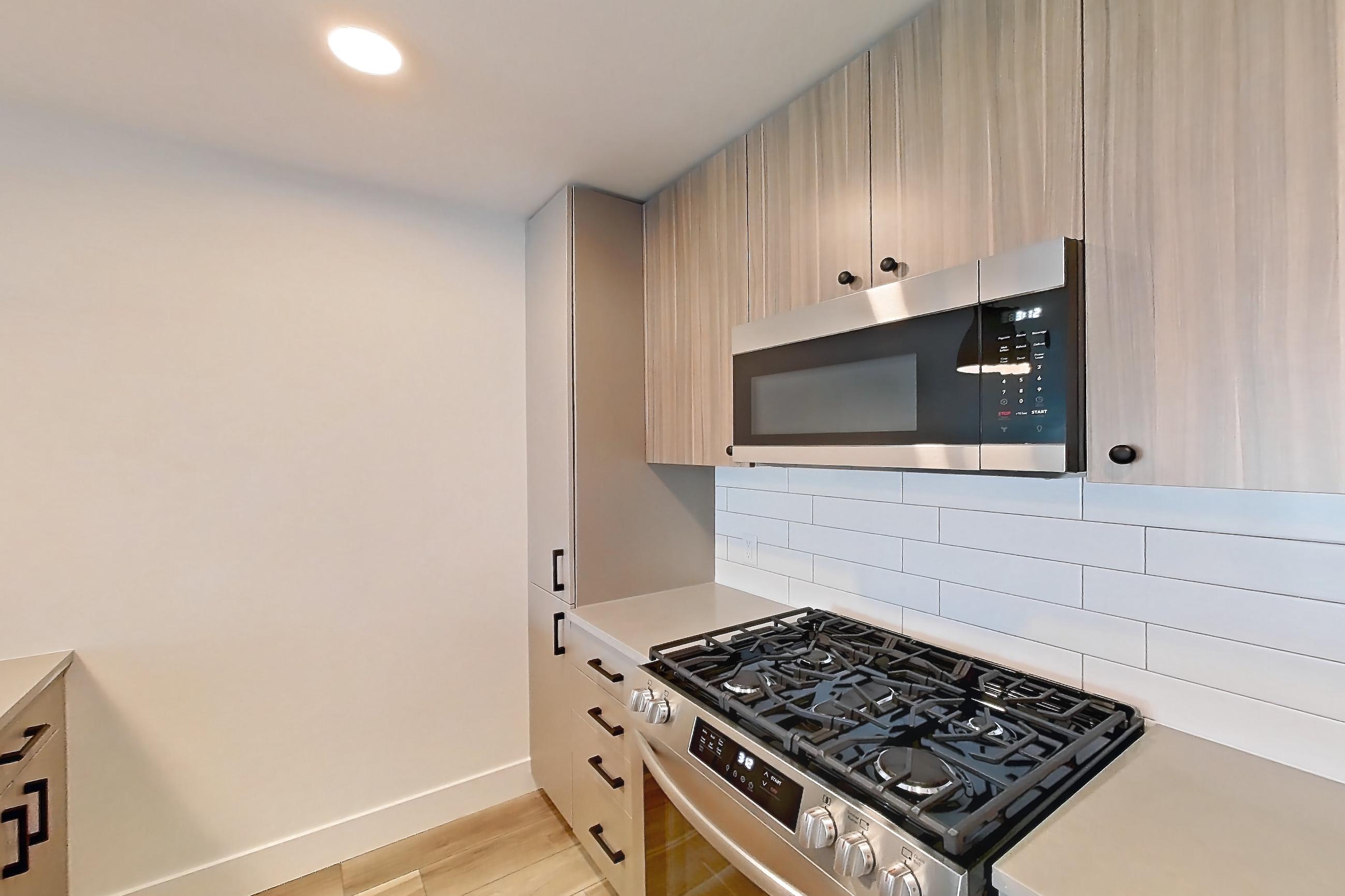 Kitchen with dishwasher, gas range, light countertops, light wood-finish flooring, oven/range, refrigerator, and stainless steel appliances, Apartment 636 at The Myles