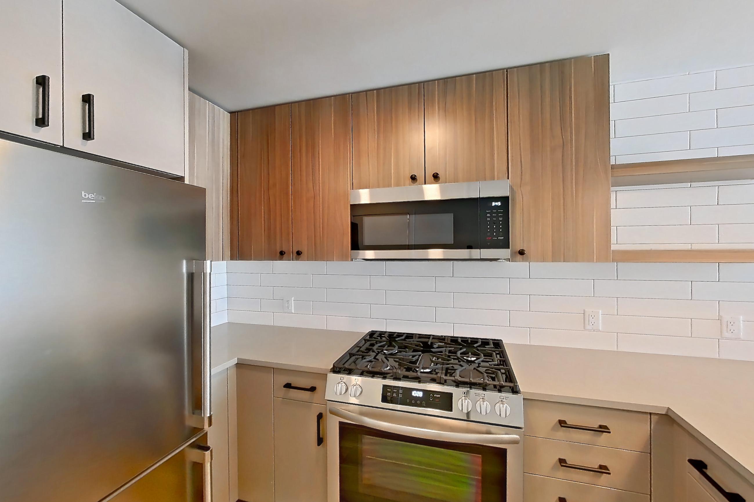 Kitchen with dishwasher, gas range, light countertops, light wood-finish flooring, oven/range, refrigerator, and stainless steel appliances, Apartment 637 at The Myles