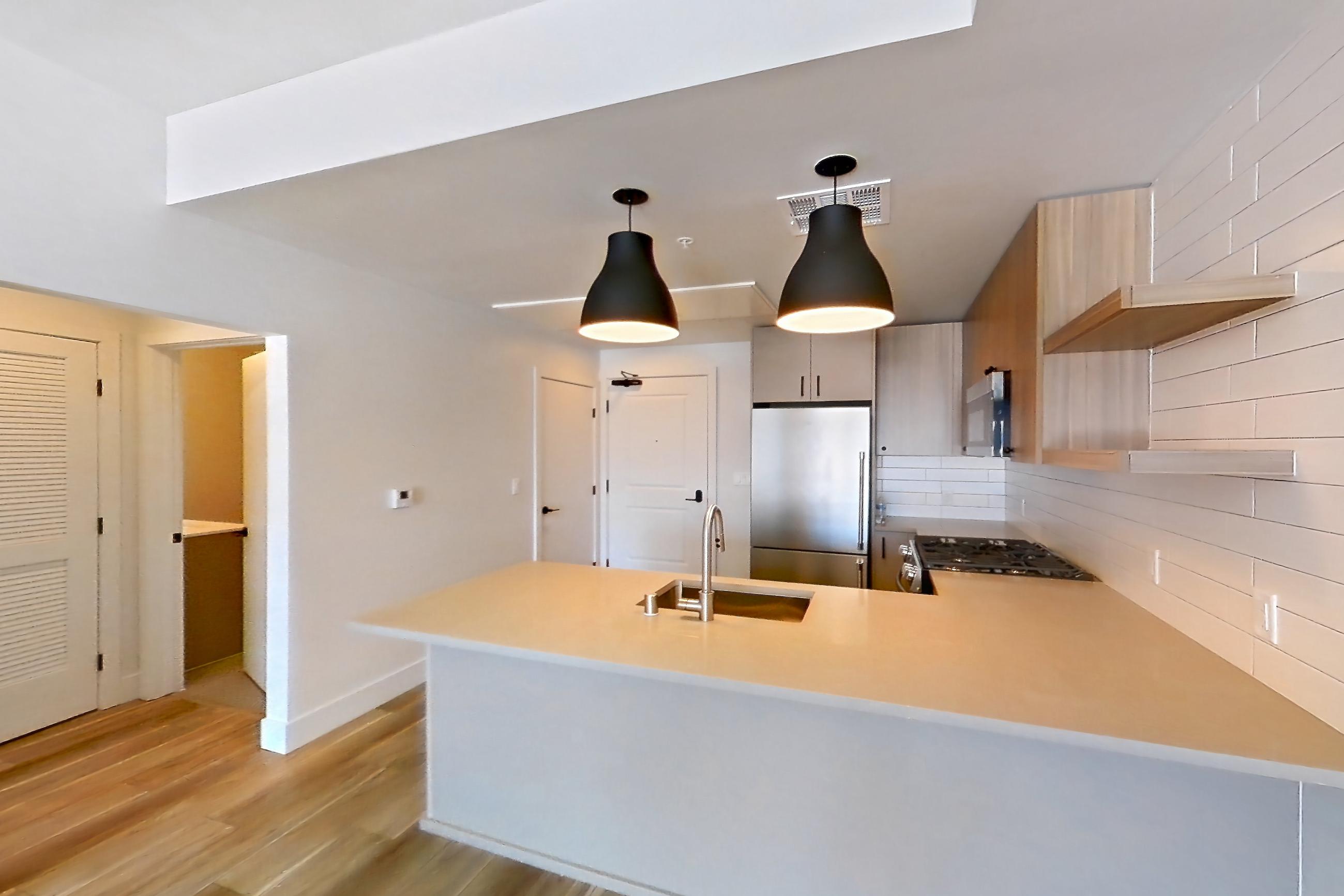 Living room with light countertops, light wood-finish flooring, refrigerator, and stainless steel appliances, Apartment 637 at The Myles