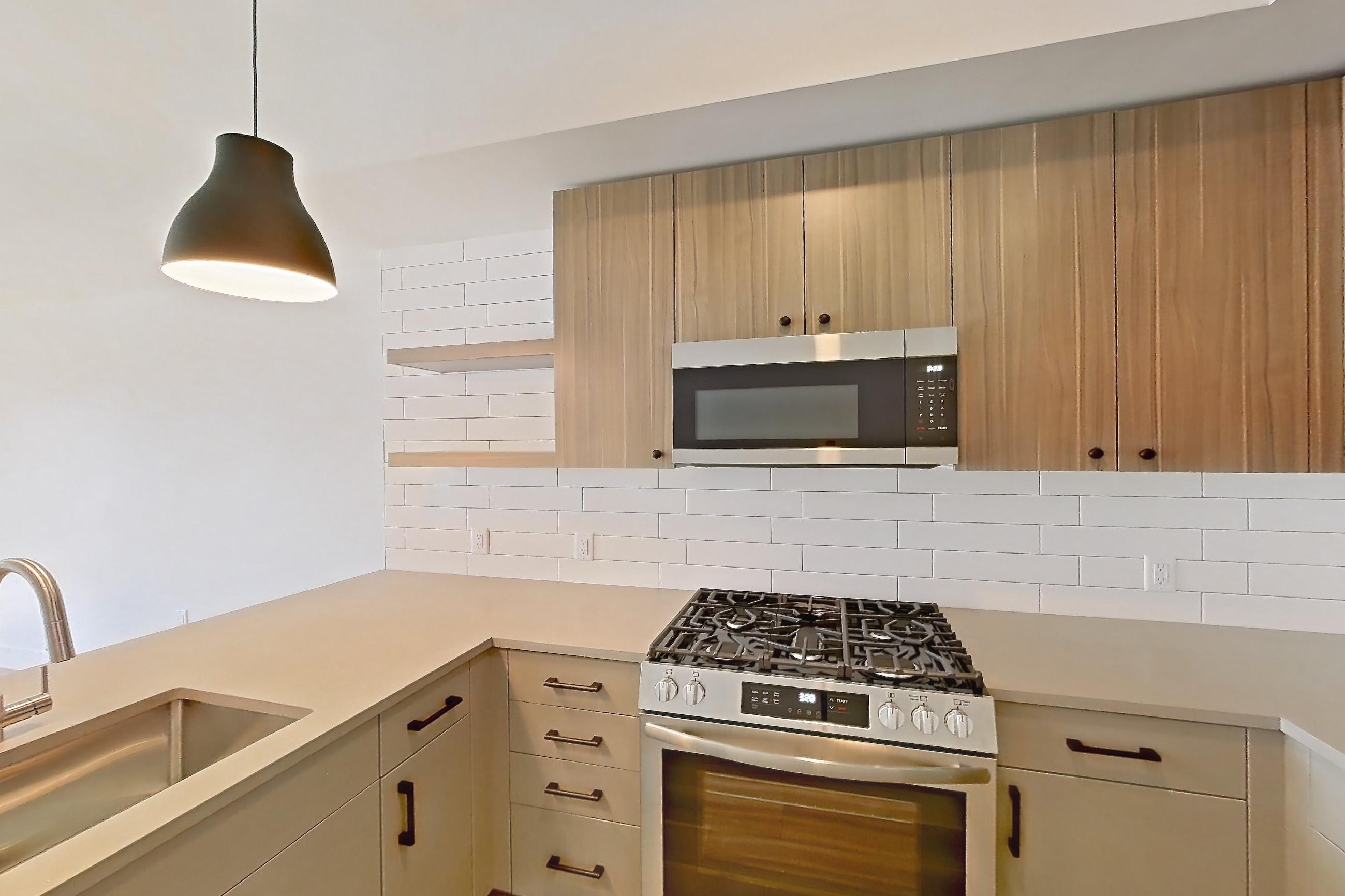Kitchen with dishwasher, gas range, light countertops, light stone countertops, light wood-finish flooring, oven/range, and stainless steel appliances, Apartment 640 at The Myles