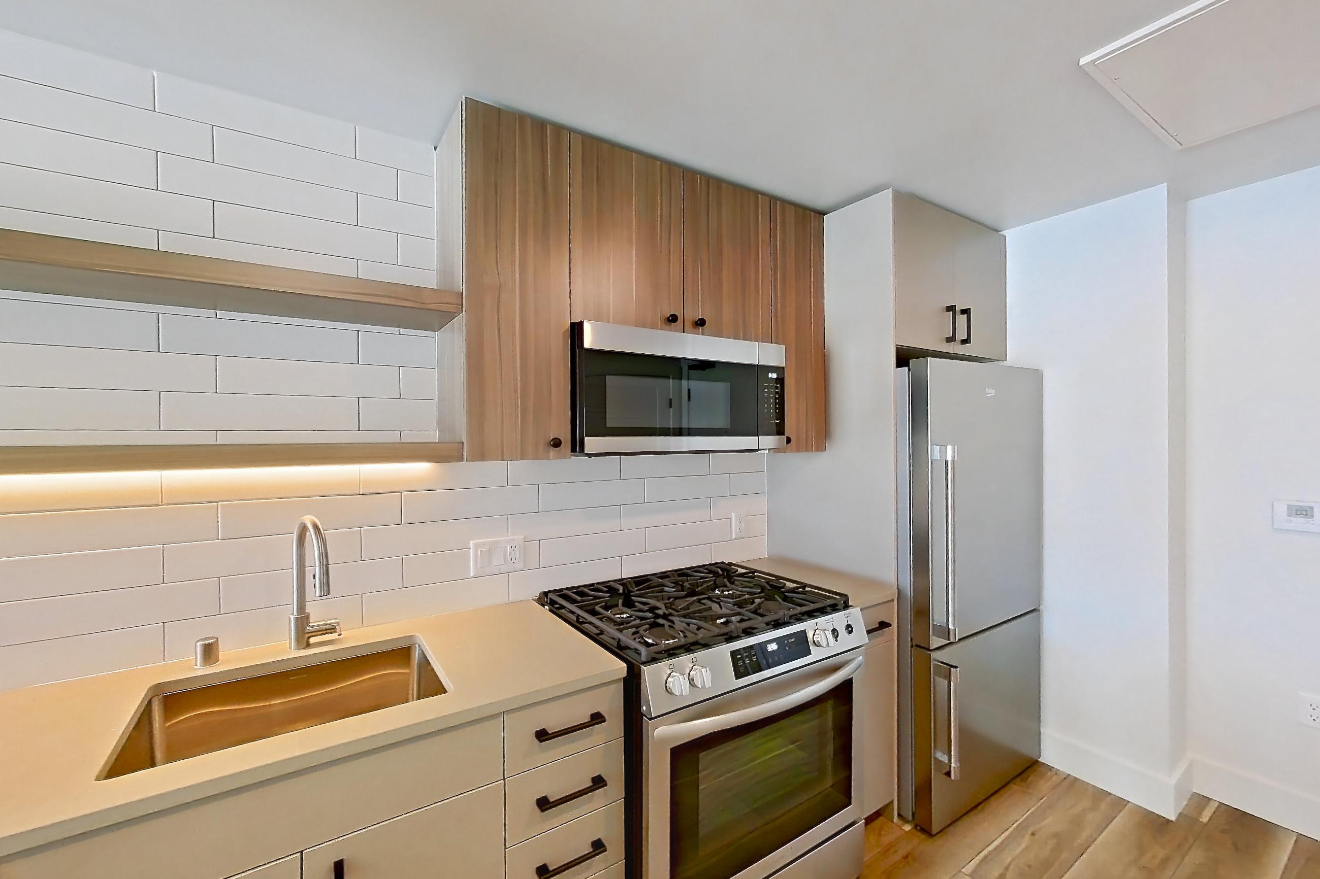 Kitchen with dishwasher, gas range, light countertops, light wood-finish flooring, microwave, oven/range, refrigerator, and stainless steel appliances, Apartment 641 at The Myles
