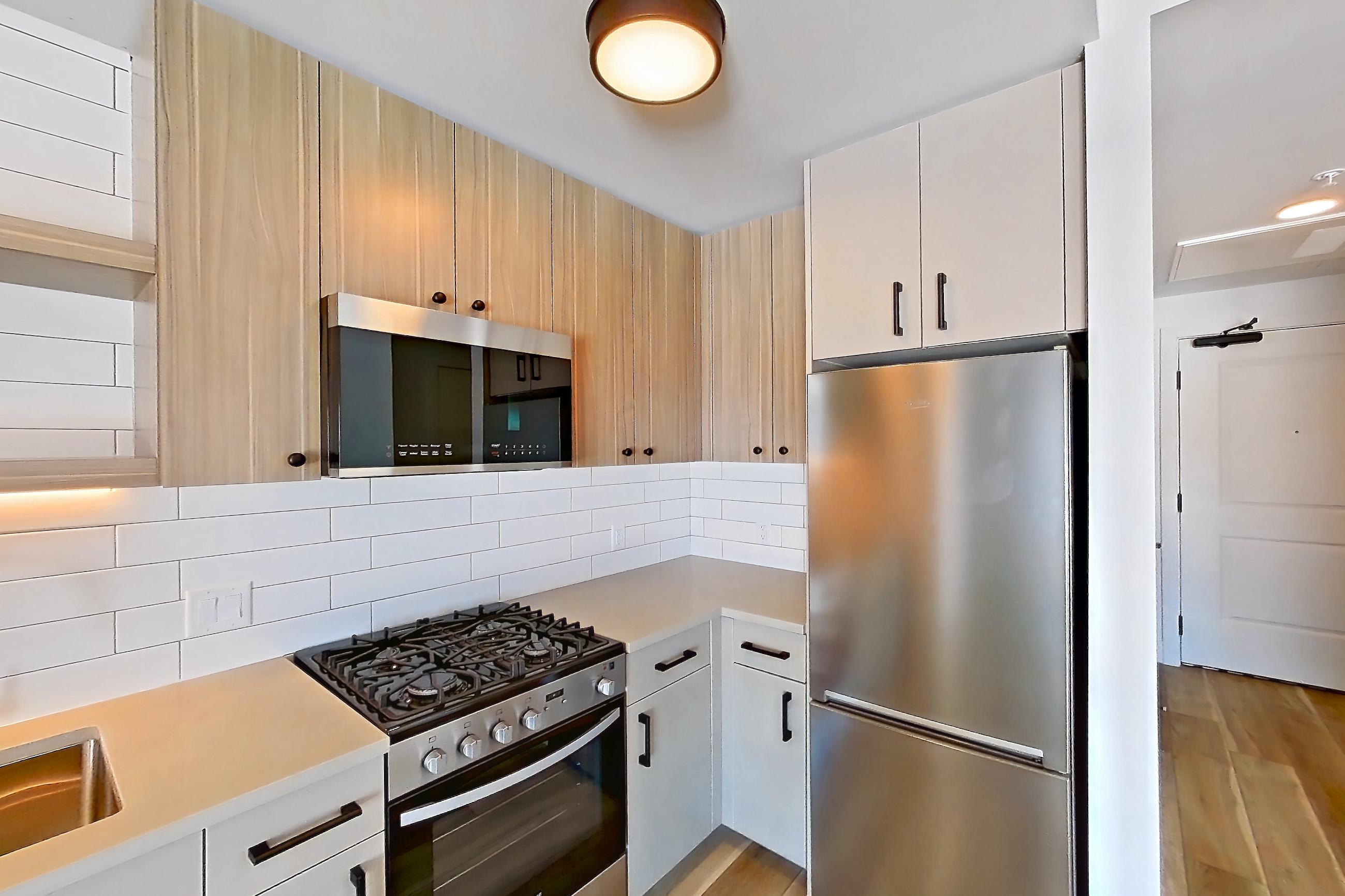Kitchen with dishwasher, gas range, light countertops, light wood-finish flooring, oven/range, refrigerator, and stainless steel appliances, Apartment 643 at The Myles
