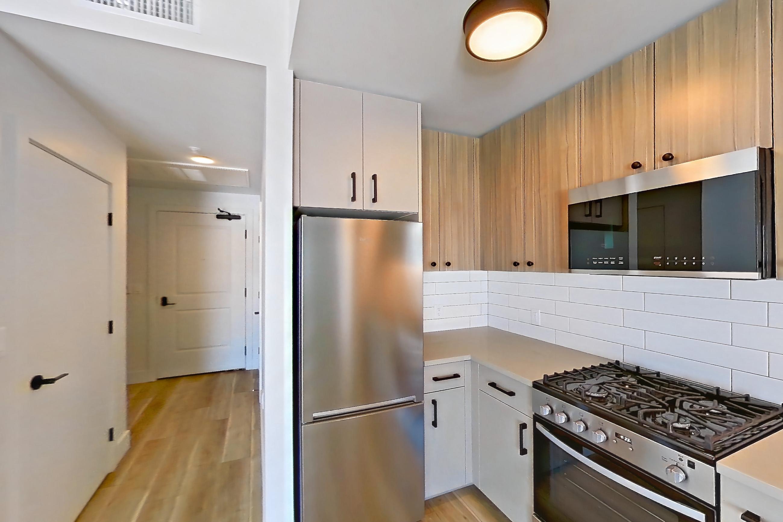 Kitchen with gas range, light countertops, light wood-finish flooring, oven/range, refrigerator, and stainless steel appliances, Apartment 645 at The Myles