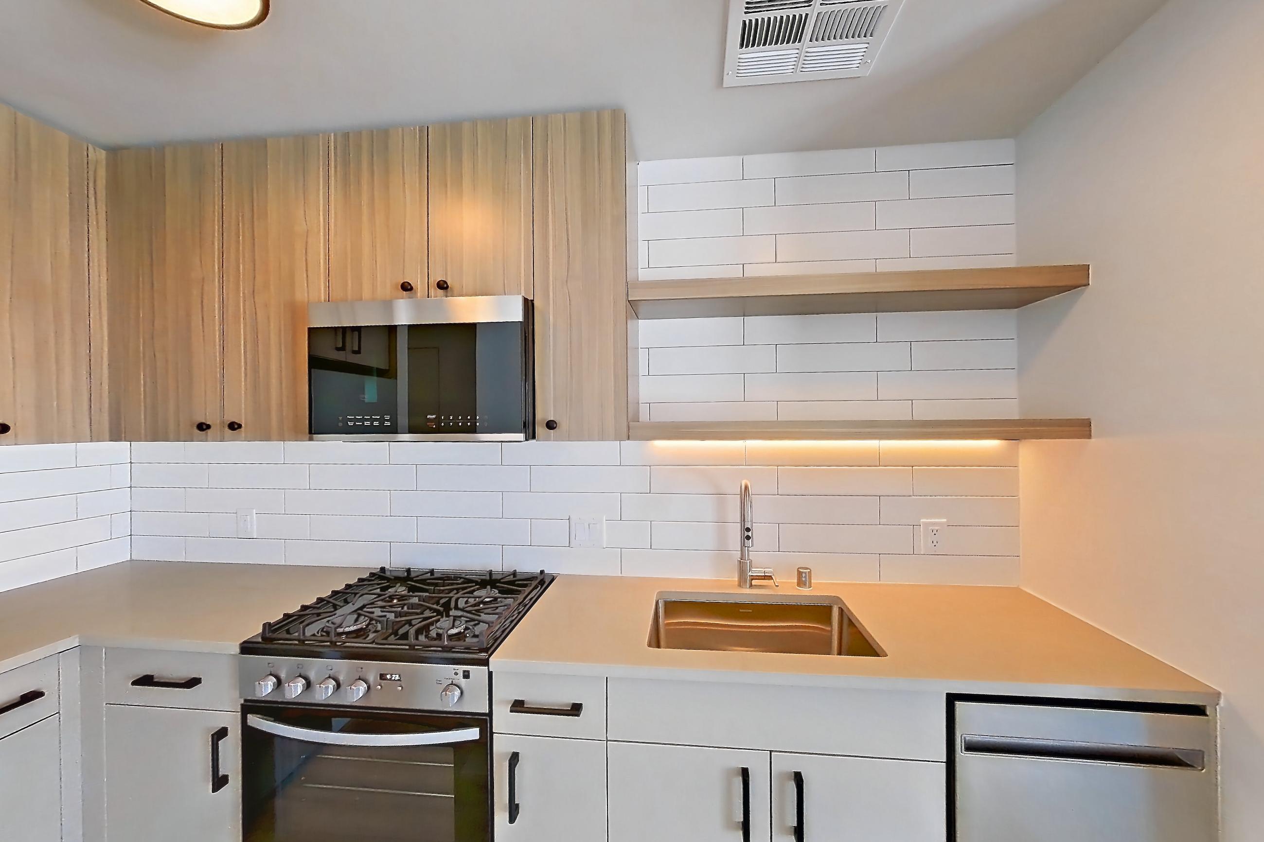 Kitchen with gas range, light countertops, light wood-finish flooring, oven/range, refrigerator, and stainless steel appliances, Apartment 645 at The Myles
