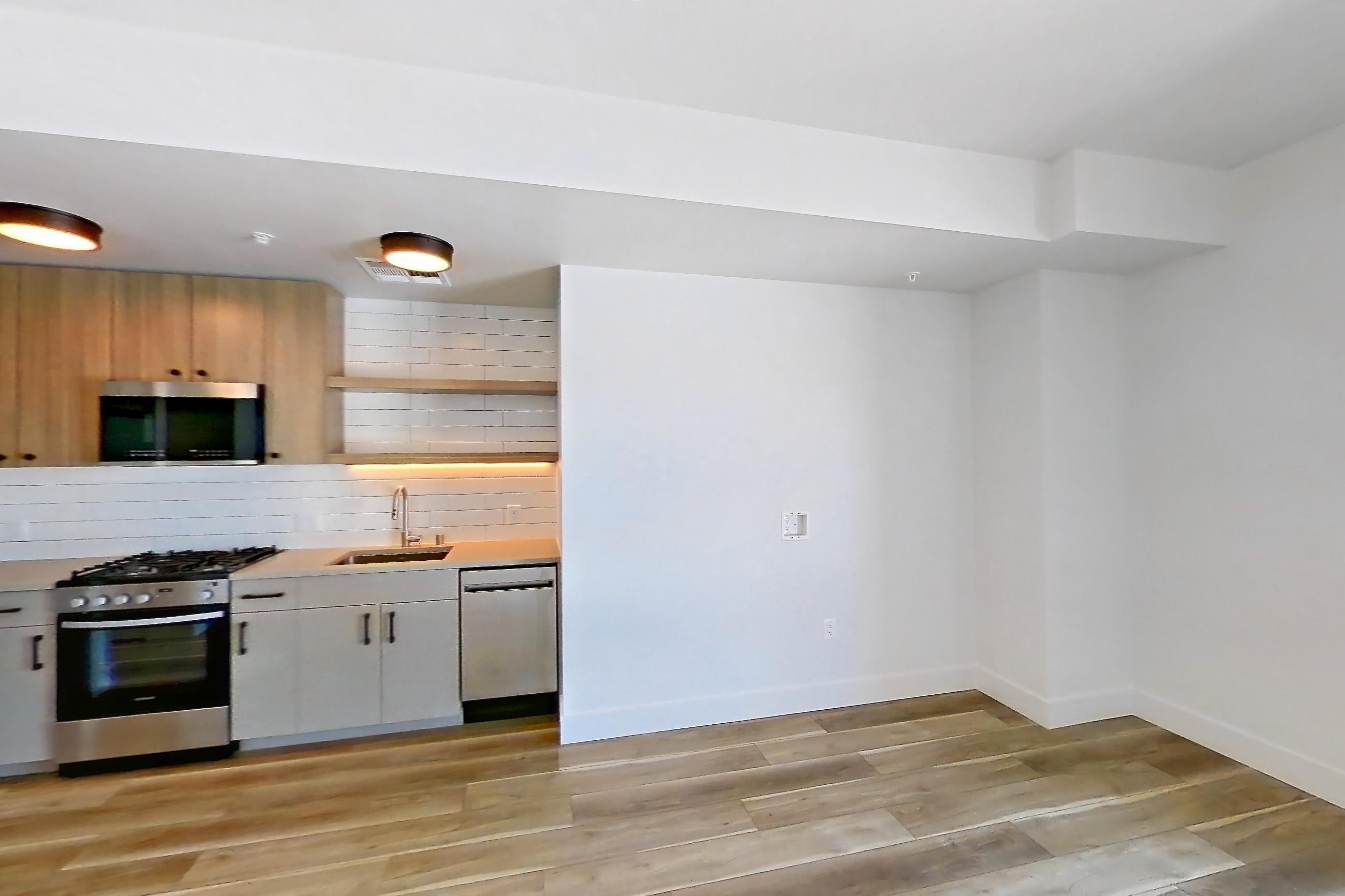 Living space with dishwasher, gas range, light countertops, light wood-finish flooring, microwave, oven/range, refrigerator, and stainless steel appliances, Apartment 645 at The Myles
