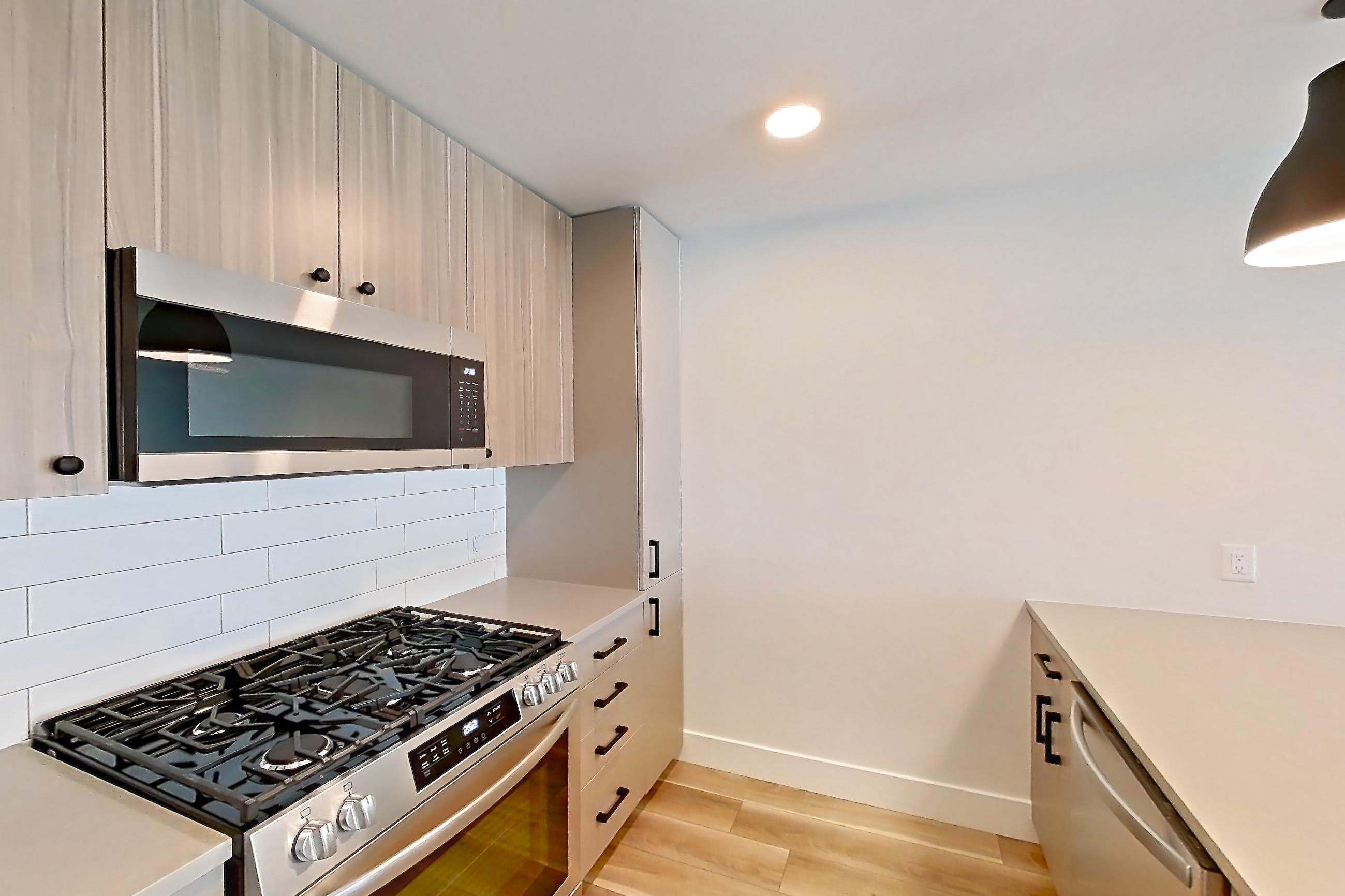 Kitchen with gas range, light countertops, light wood-finish flooring, oven/range, refrigerator, and stainless steel appliances, Apartment 646 at The Myles