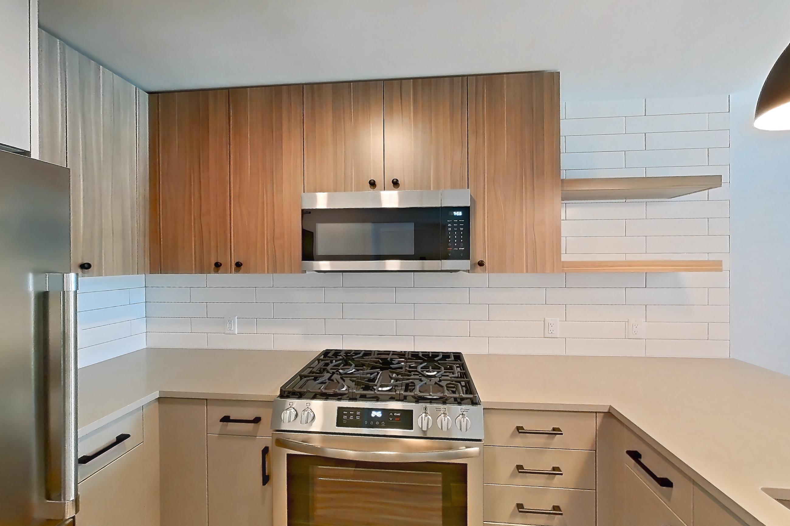 Kitchen with dishwasher, gas range, light countertops, light wood-finish flooring, microwave, oven/range, refrigerator, and stainless steel appliances, Apartment 647 at The Myles