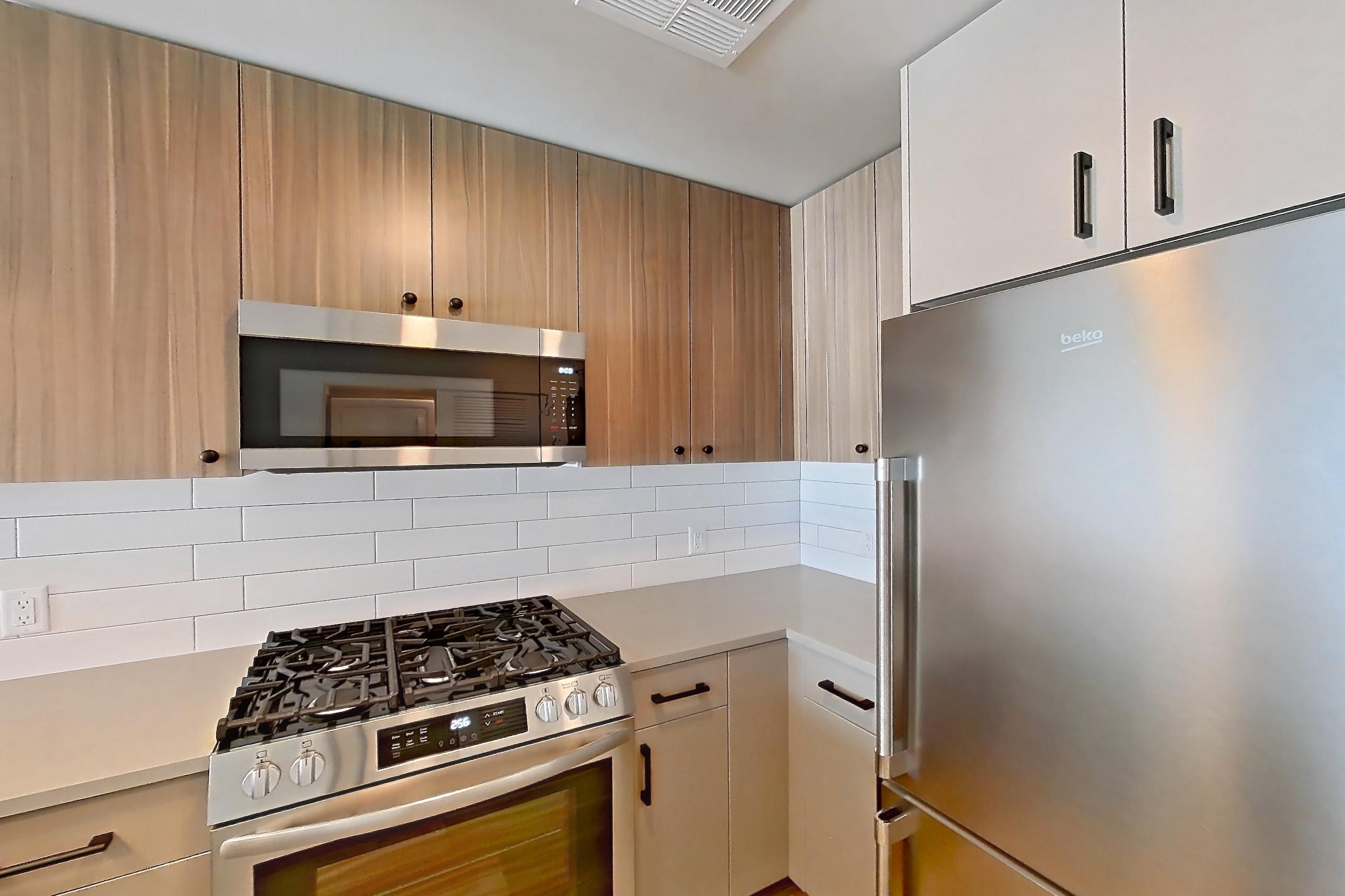 Kitchen with dishwasher, gas range, light countertops, light wood-finish flooring, oven/range, refrigerator, and stainless steel appliances, Apartment 648 at The Myles