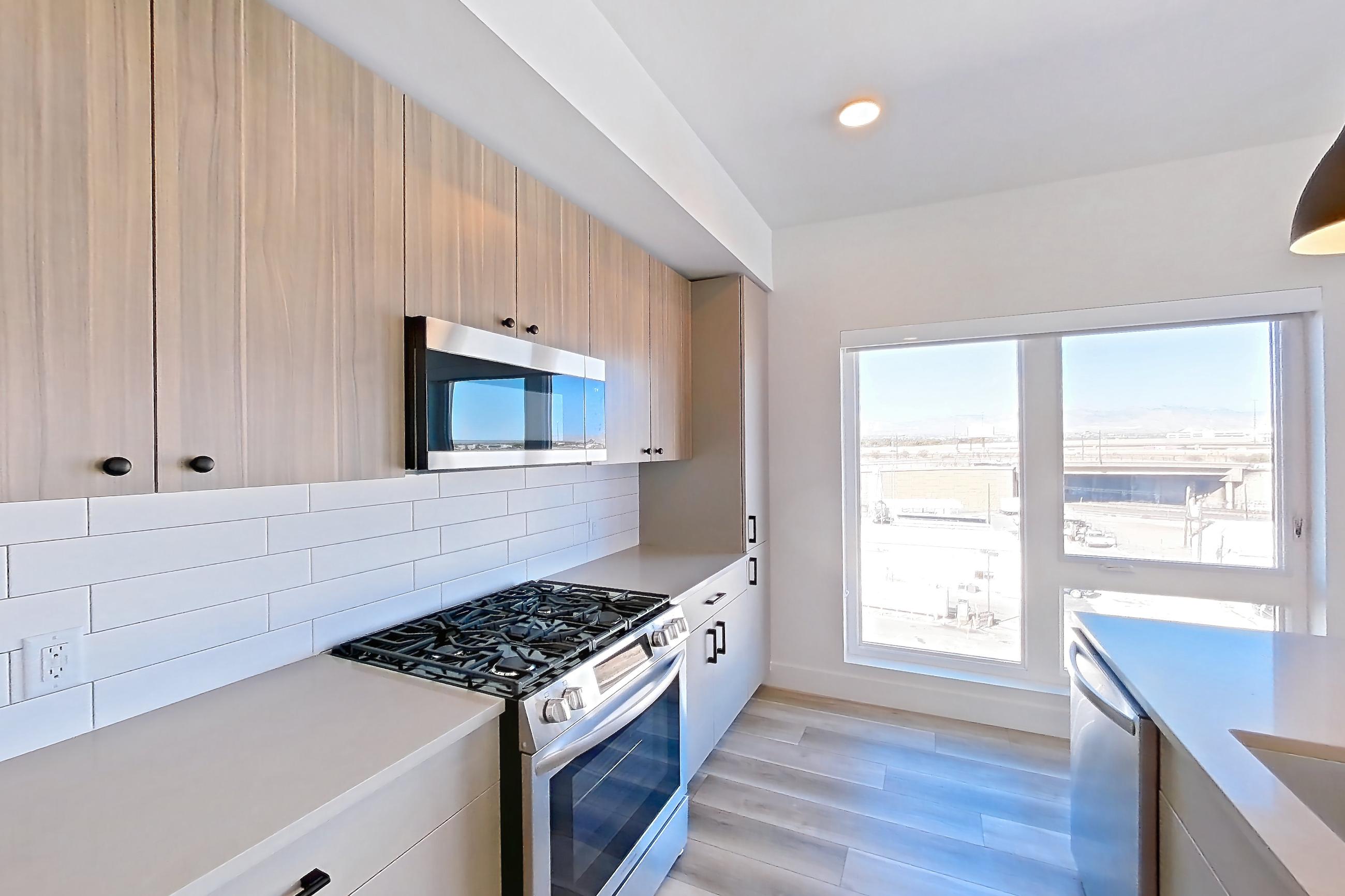 Kitchen with gas range, kitchen island, light countertops, light stone countertops, light wood-finish flooring, oven/range, and stainless steel appliances, Apartment 649 at The Myles