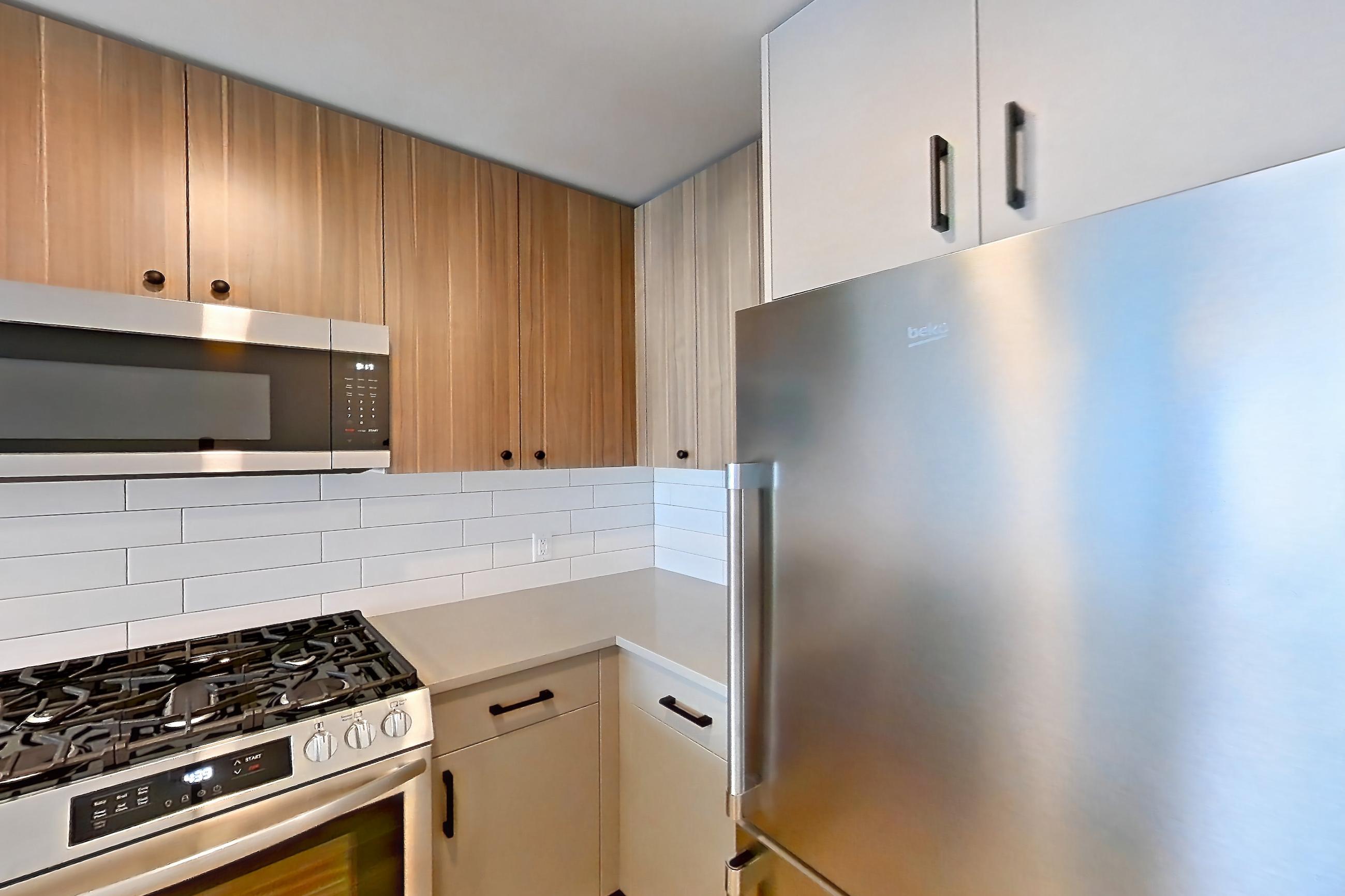Kitchen with dishwasher, gas range, light countertops, light wood-finish flooring, oven/range, refrigerator, and stainless steel appliances, Apartment 650 at The Myles
