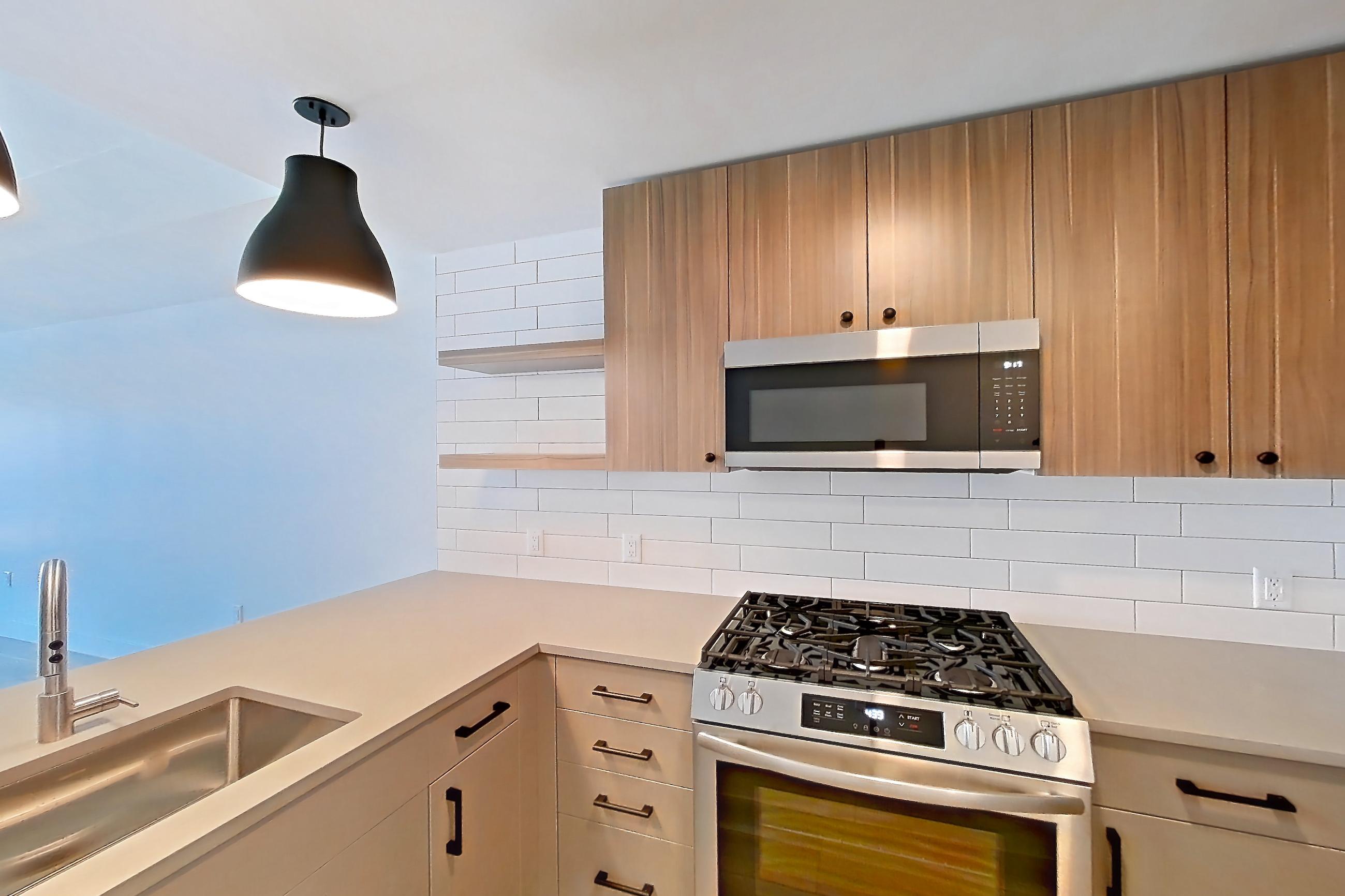 Kitchen with dishwasher, gas range, light countertops, light wood-finish flooring, oven/range, refrigerator, and stainless steel appliances, Apartment 650 at The Myles