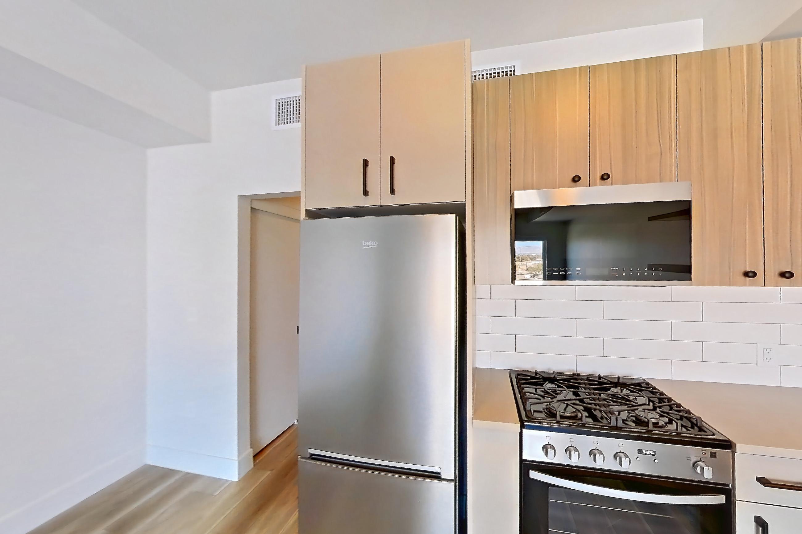 Kitchen with dishwasher, gas range, light countertops, light wood-finish flooring, oven/range, refrigerator, and stainless steel appliances, Apartment 651 at The Myles
