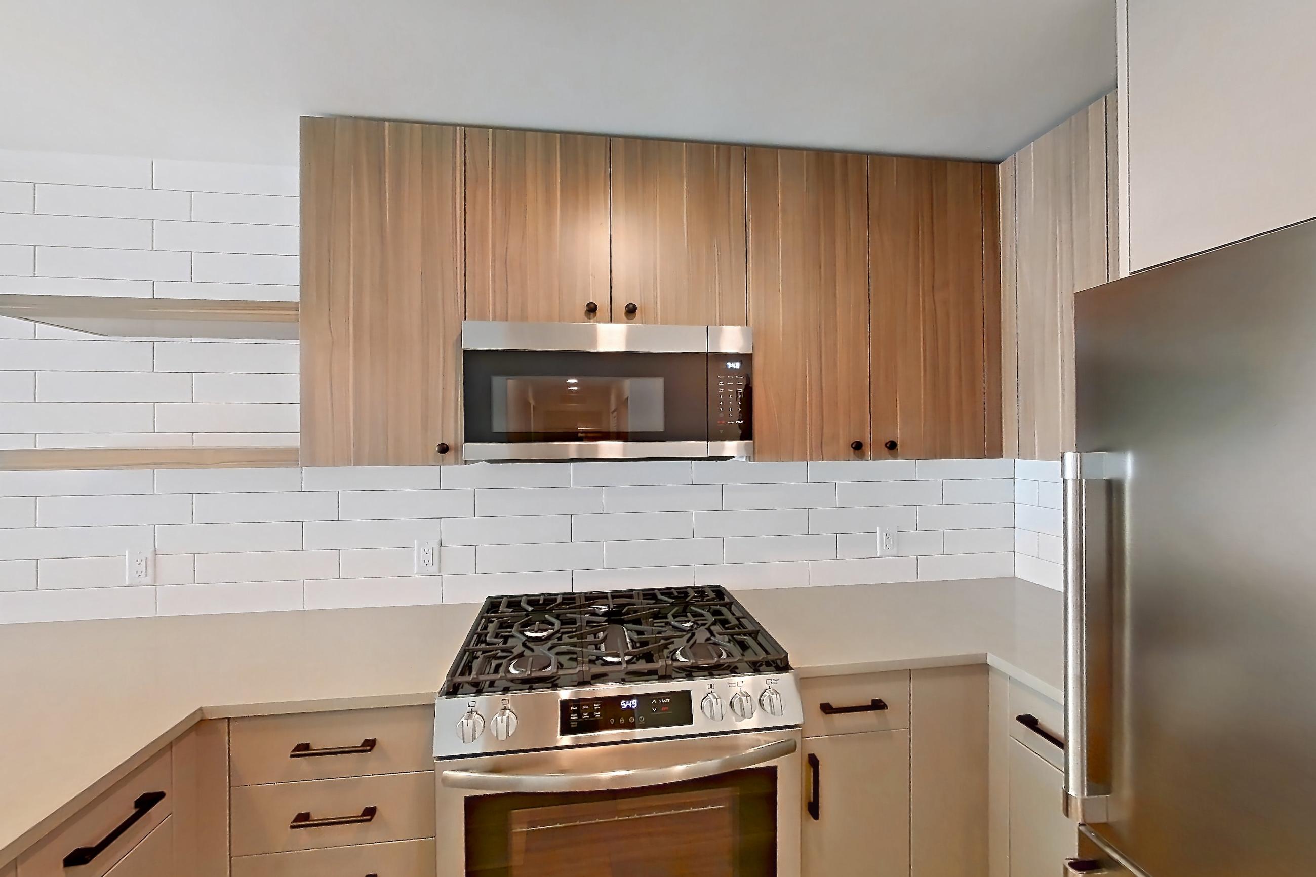 Kitchen with dishwasher, gas range, light countertops, light wood-finish flooring, microwave, oven/range, refrigerator, stainless steel appliances, and wood-look tile flooring, Apartment 652 at The Myles