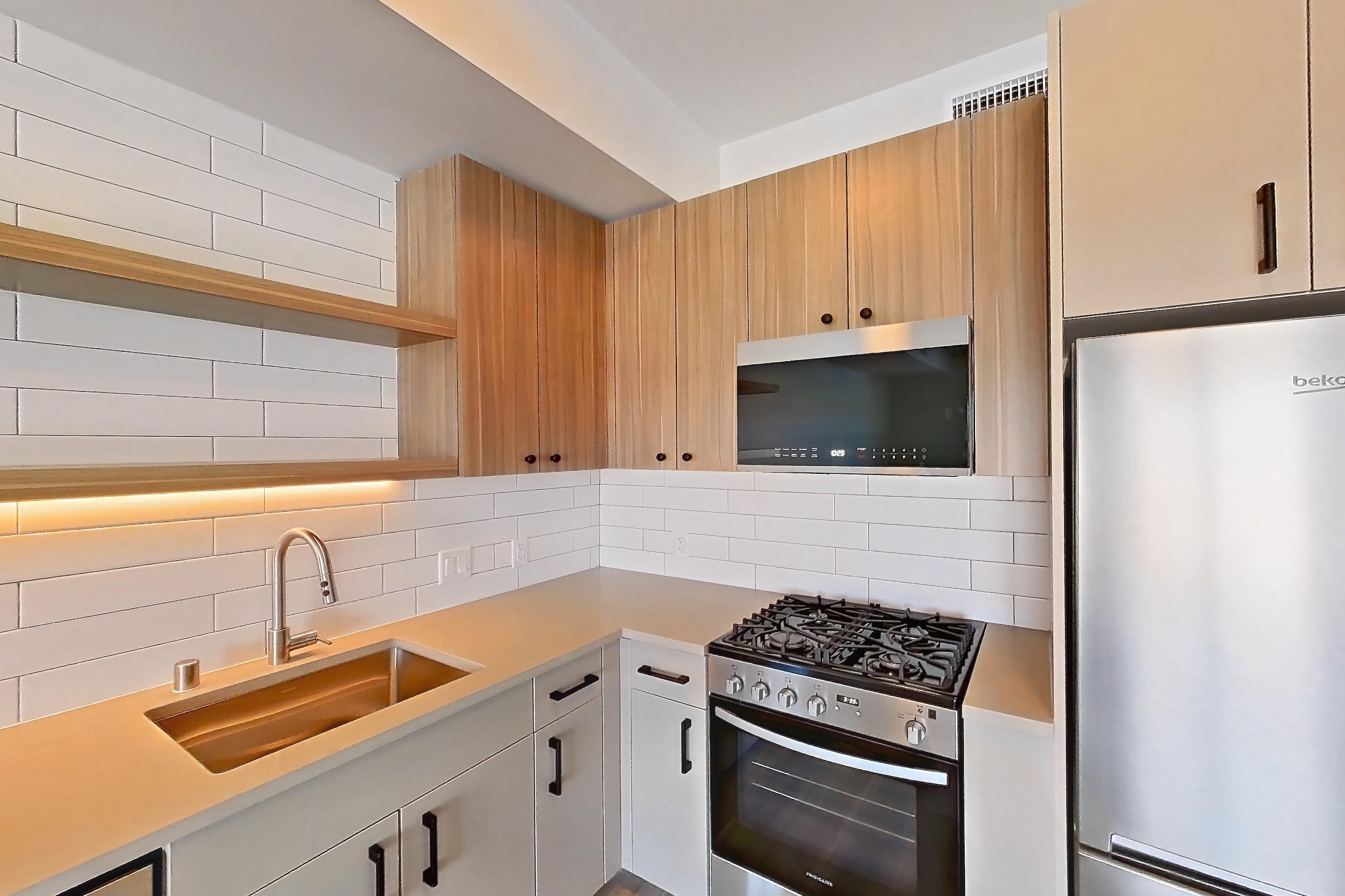 Kitchen with gas range, light countertops, light wood-finish flooring, oven/range, refrigerator, and stainless steel appliances, Apartment 653 at The Myles