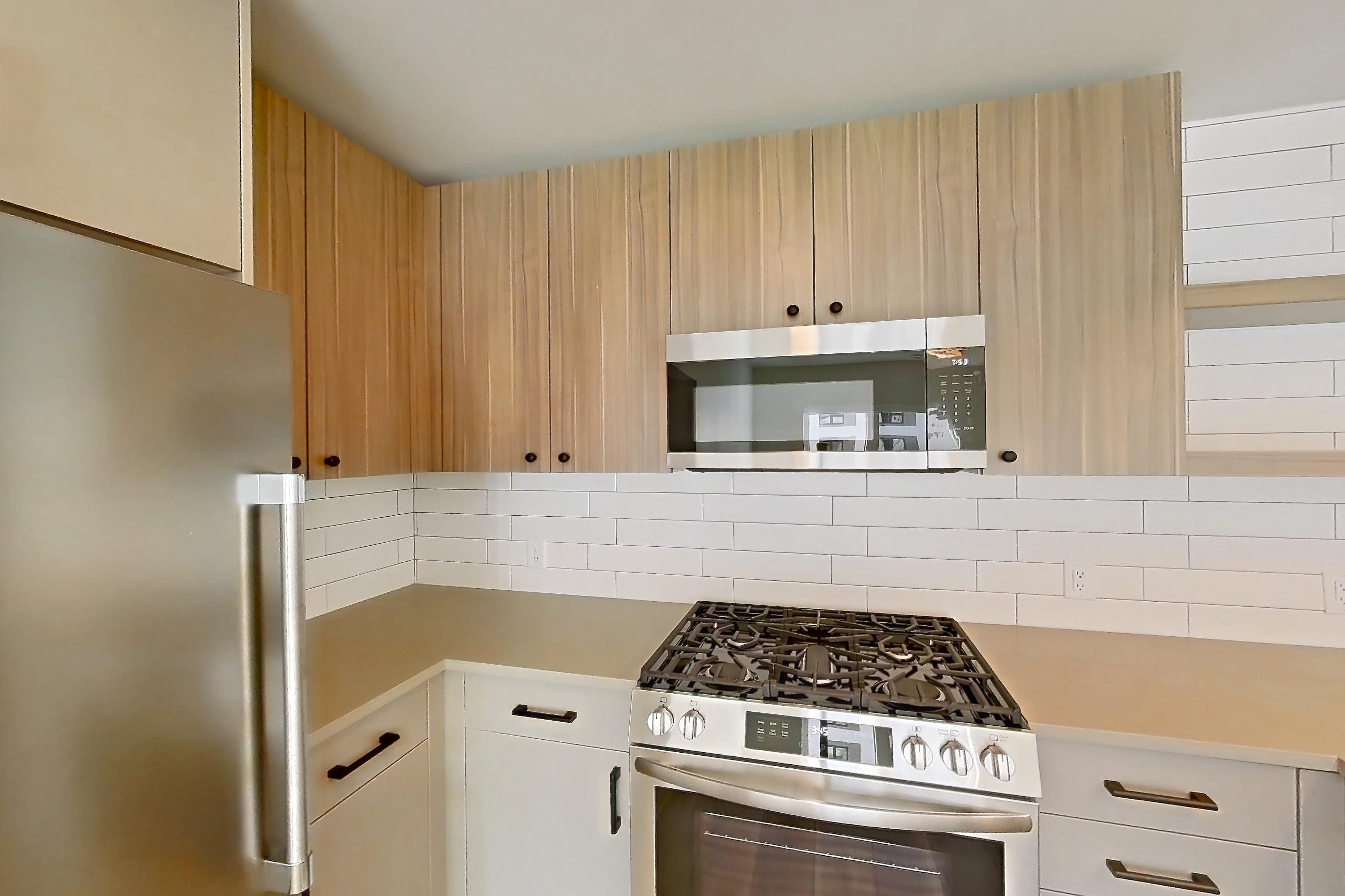 Kitchen with dishwasher, gas range, light countertops, light wood-finish flooring, oven/range, refrigerator, and stainless steel appliances, Apartment 654 at The Myles