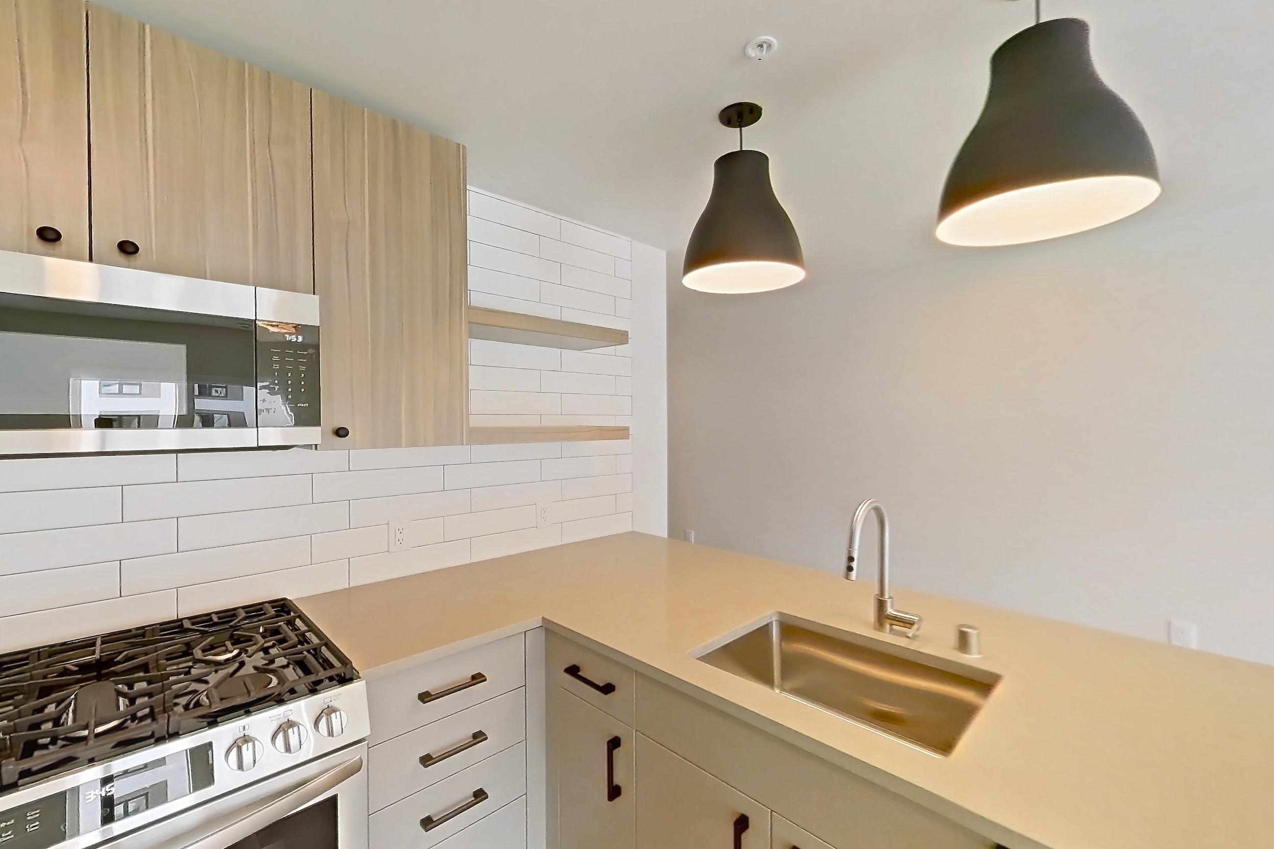 Kitchen with dishwasher, gas range, light countertops, light wood-finish flooring, oven/range, refrigerator, and stainless steel appliances, Apartment 654 at The Myles