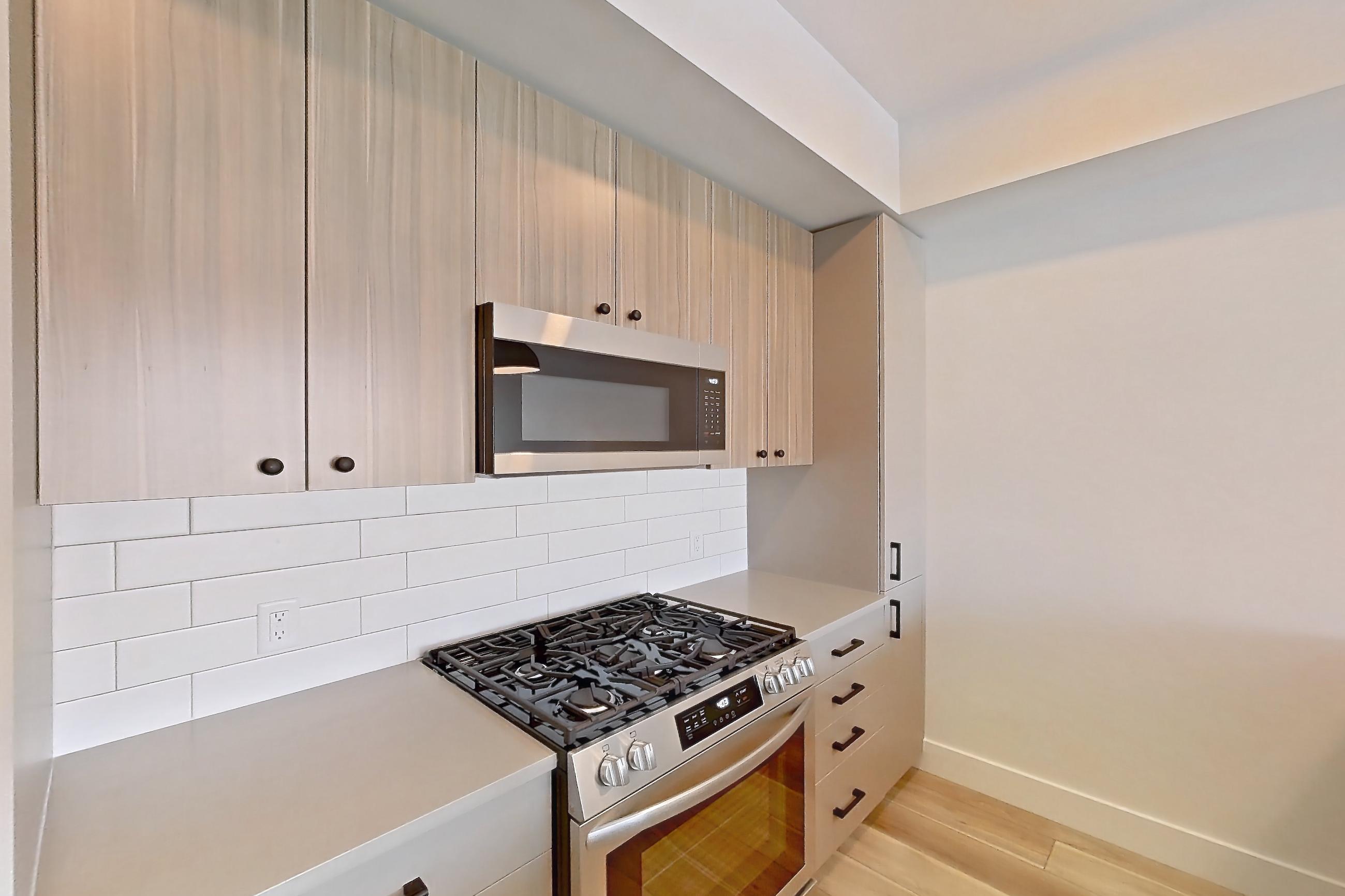 Kitchen with dishwasher, gas range, light countertops, light wood-finish flooring, microwave, oven/range, and stainless steel appliances, Apartment 655 at The Myles
