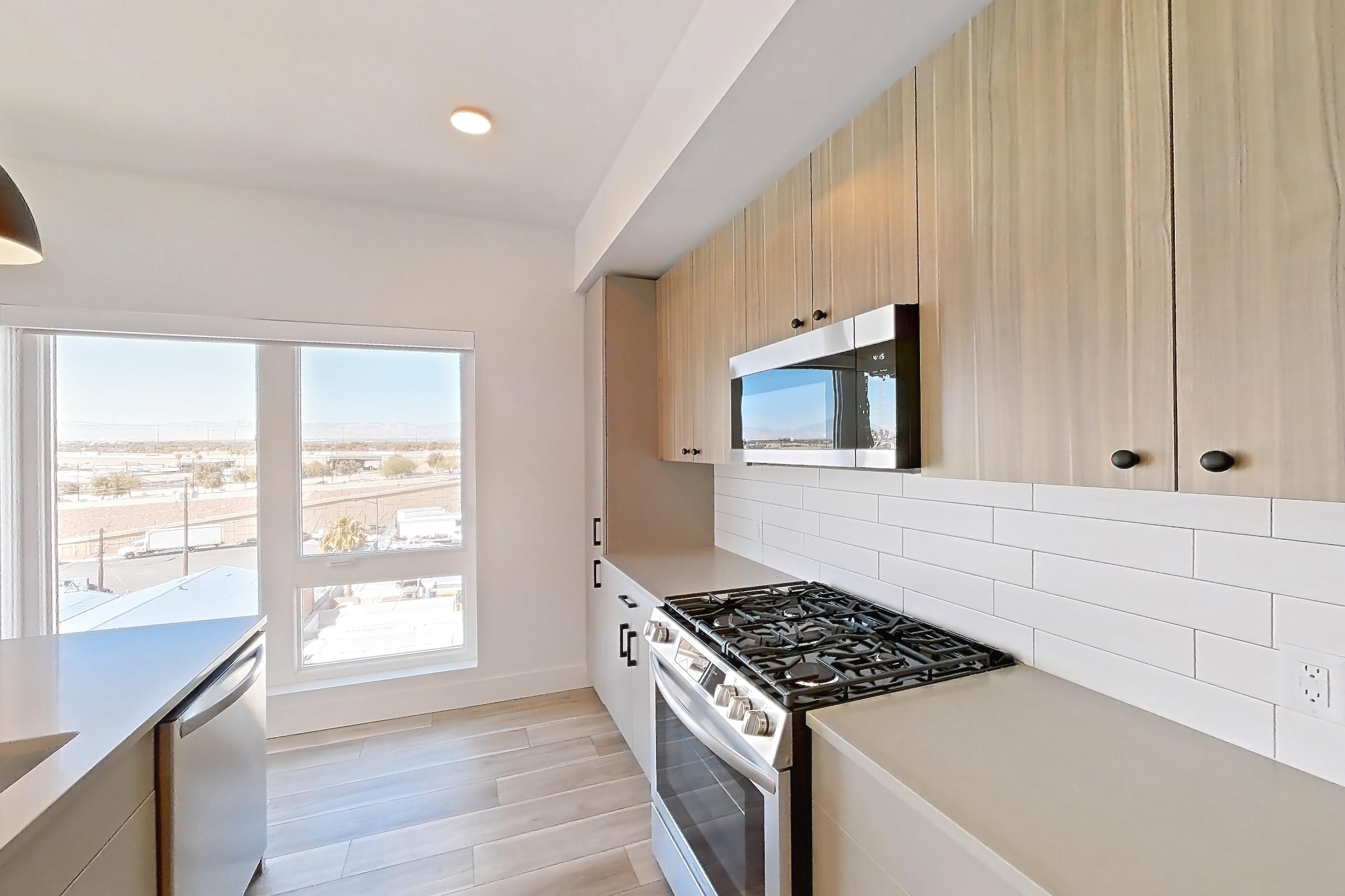 Kitchen with gas range, kitchen island, light countertops, light stone countertops, light wood-finish flooring, oven/range, and stainless steel appliances, Apartment 656 at The Myles