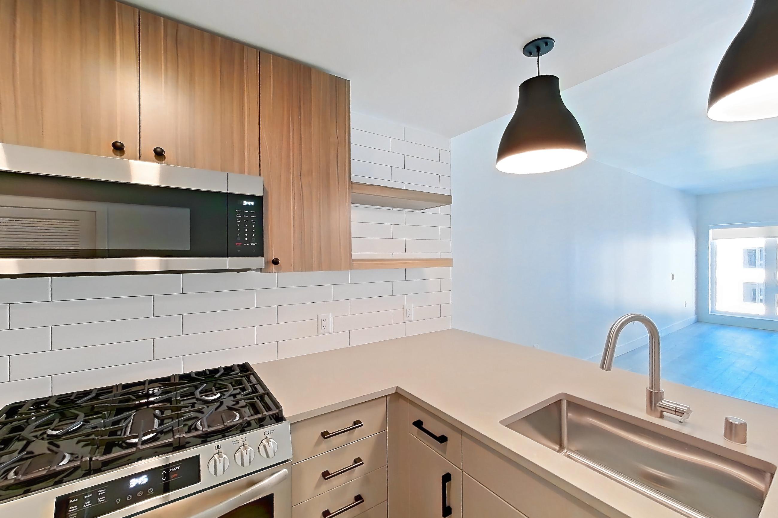 Kitchen with dishwasher, gas range, light countertops, light wood-finish flooring, microwave, oven/range, refrigerator, and stainless steel appliances, Apartment 702 at The Myles