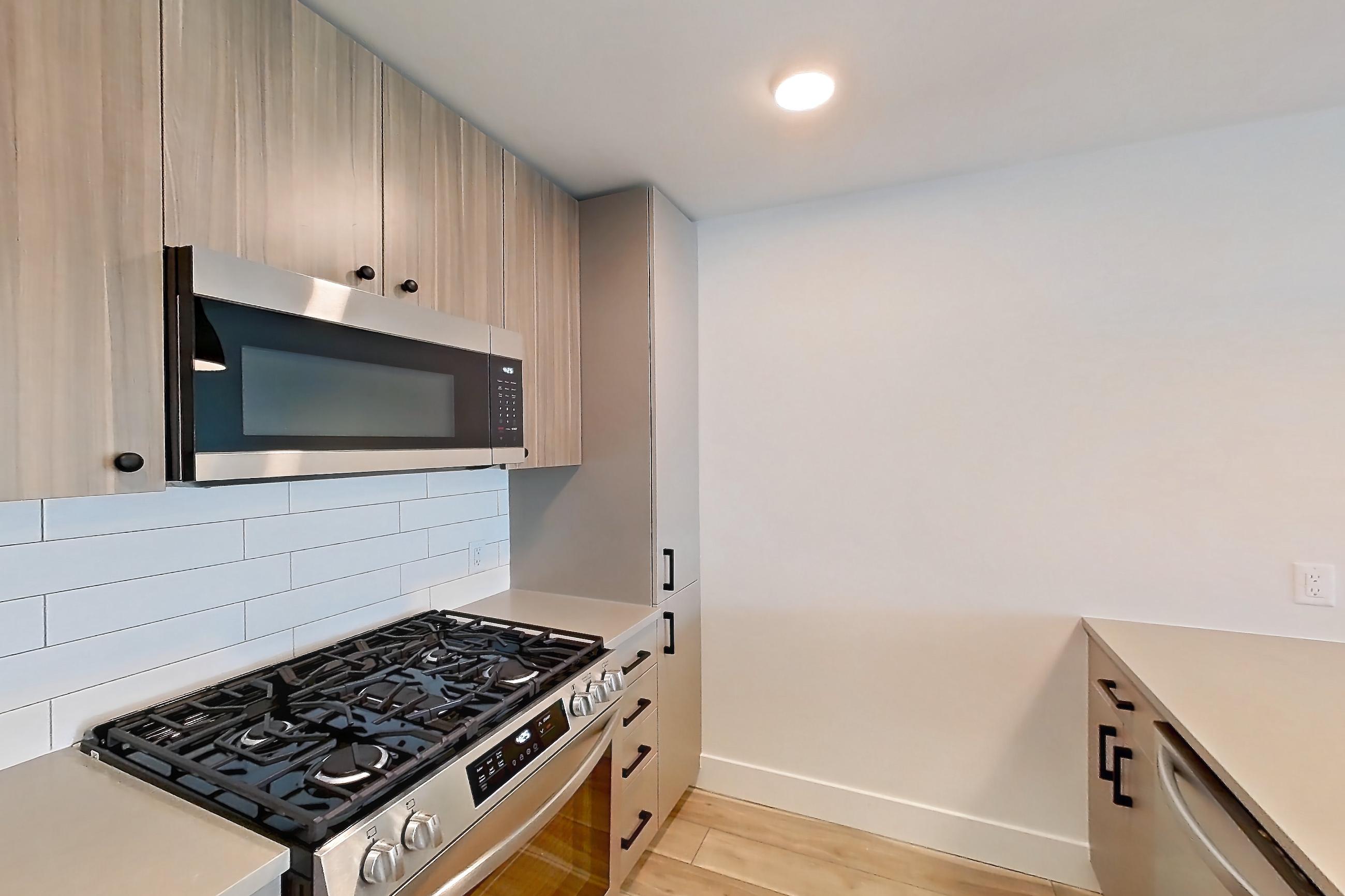 Kitchen with dishwasher, gas range, light countertops, light wood-finish flooring, microwave, oven/range, refrigerator, and stainless steel appliances, Apartment 703 at The Myles