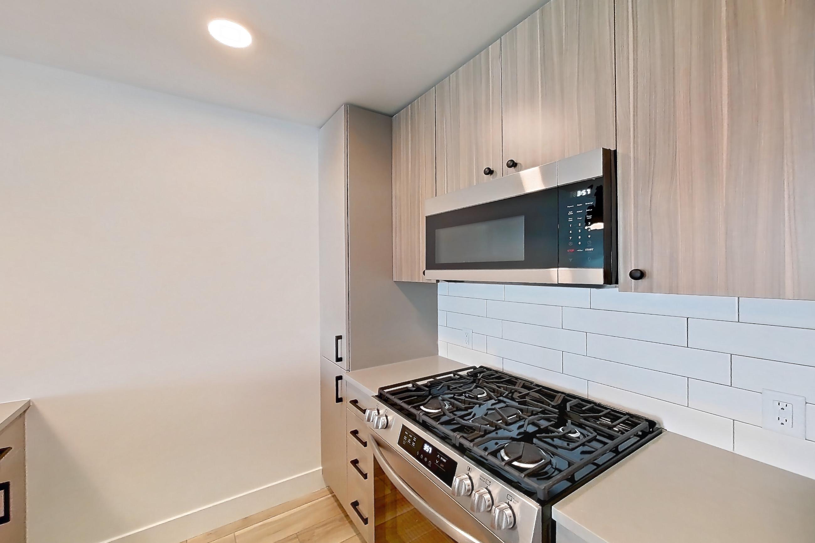 Kitchen with dishwasher, gas range, light countertops, light wood-finish flooring, microwave, oven/range, and stainless steel appliances, Apartment 704 at The Myles