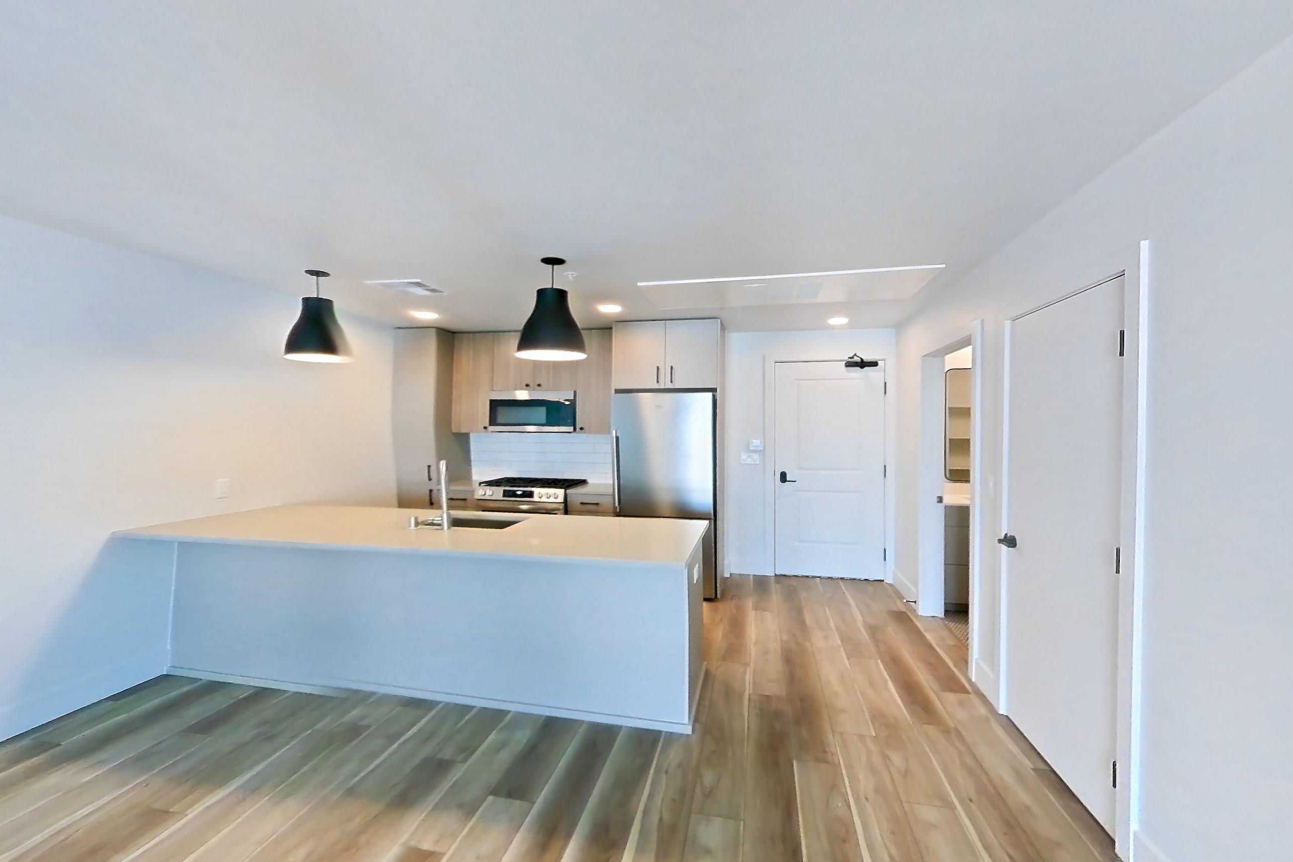 Living room with gas range, light countertops, light wood-finish flooring, oven/range, range hood, refrigerator, and stainless steel appliances, Apartment 704 at The Myles