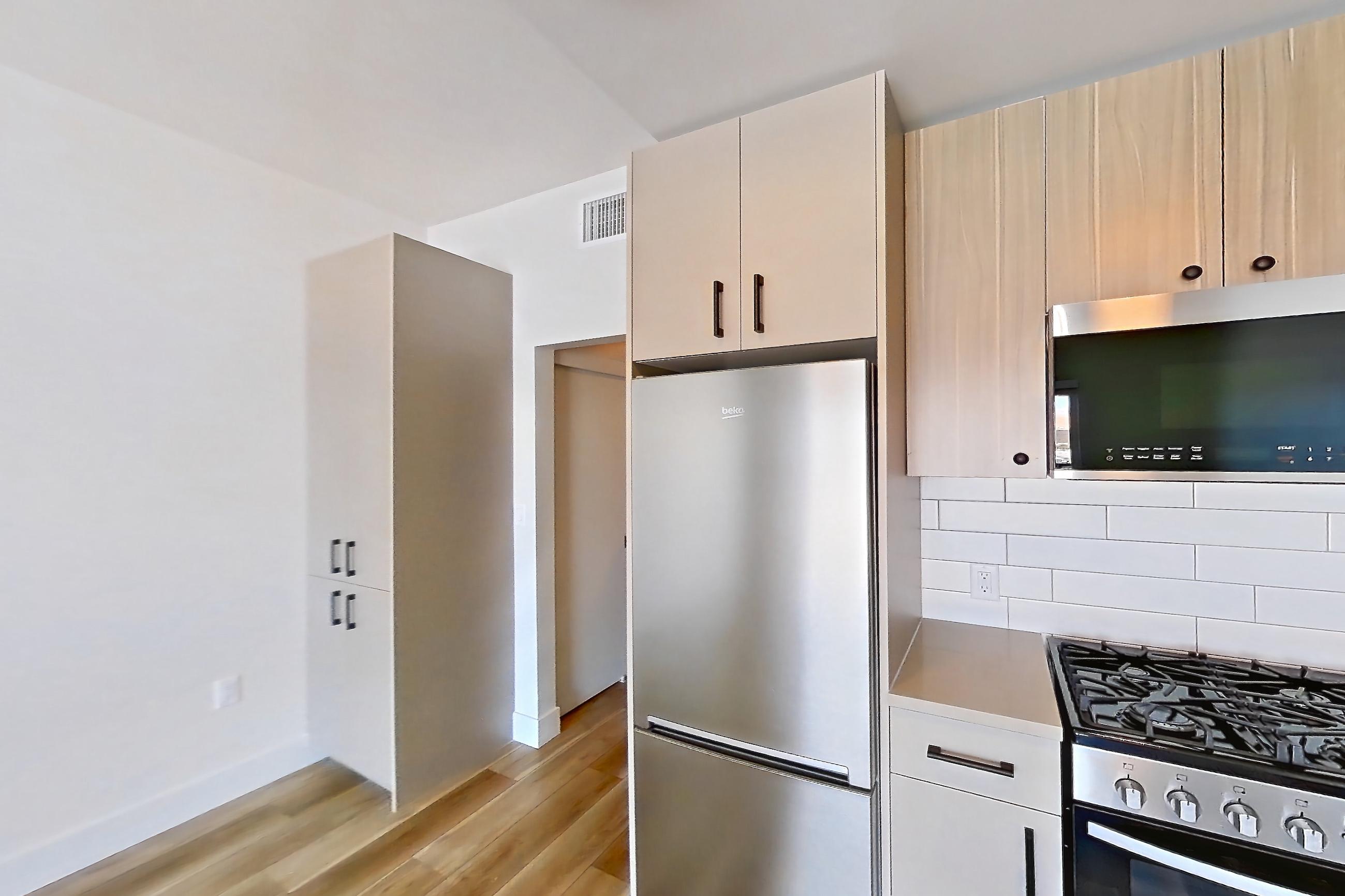 Kitchen with dishwasher, gas range, light countertops, light wood-finish flooring, oven/range, refrigerator, and stainless steel appliances, Apartment 708 at The Myles