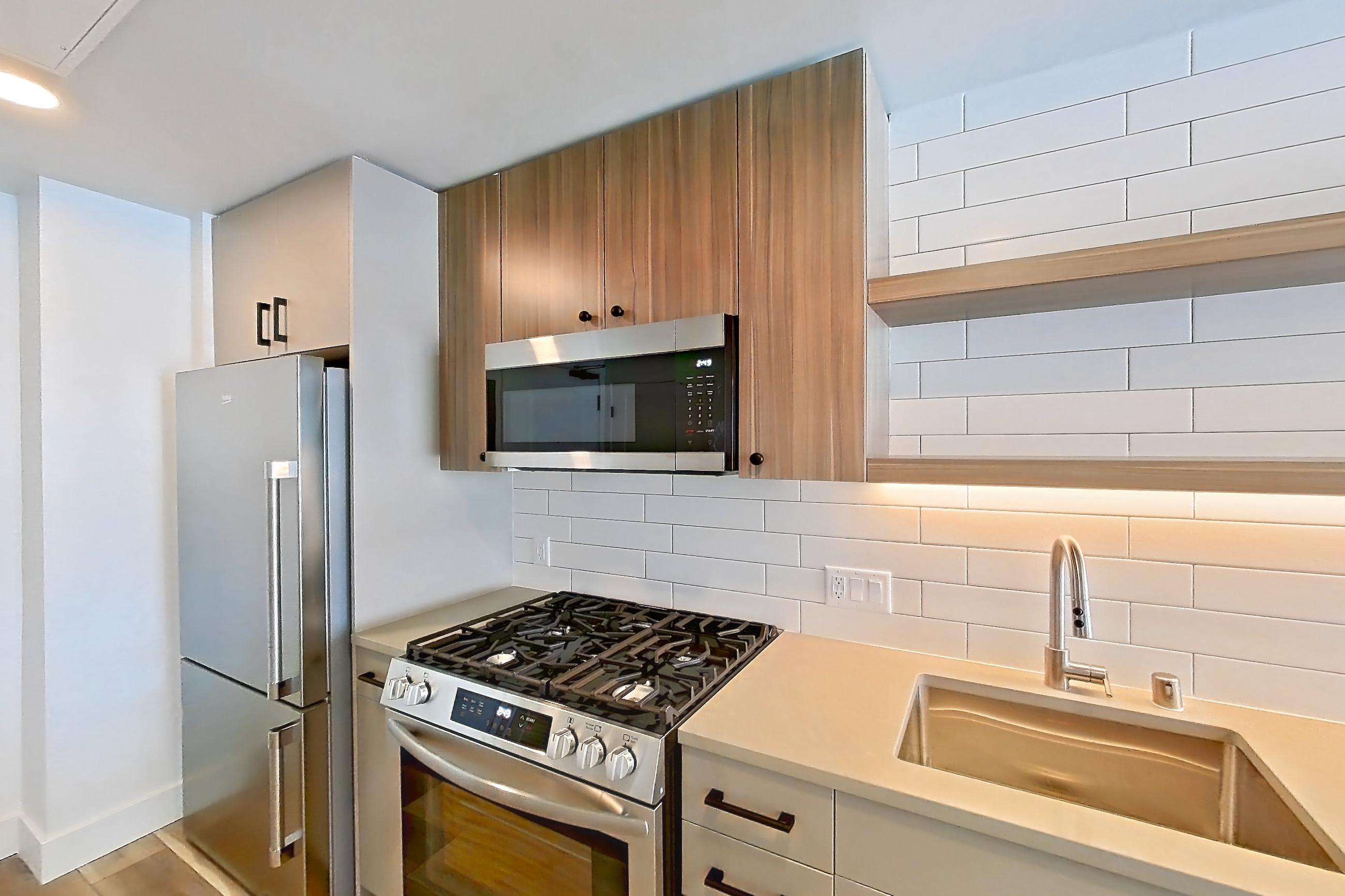 Kitchen with dishwasher, gas range, light countertops, light wood-finish flooring, microwave, oven/range, refrigerator, and stainless steel appliances, Apartment 709 at The Myles