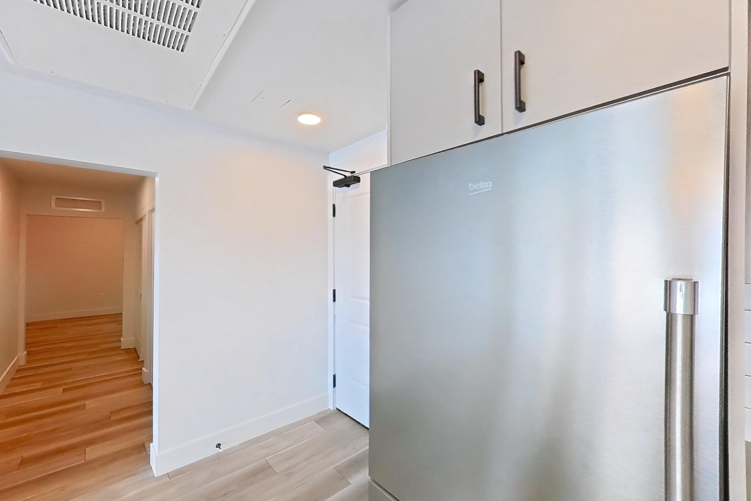 Kitchen with gas range, kitchen island, light countertops, light wood-finish flooring, oven/range, refrigerator, and stainless steel appliances, Apartment 711 at The Myles