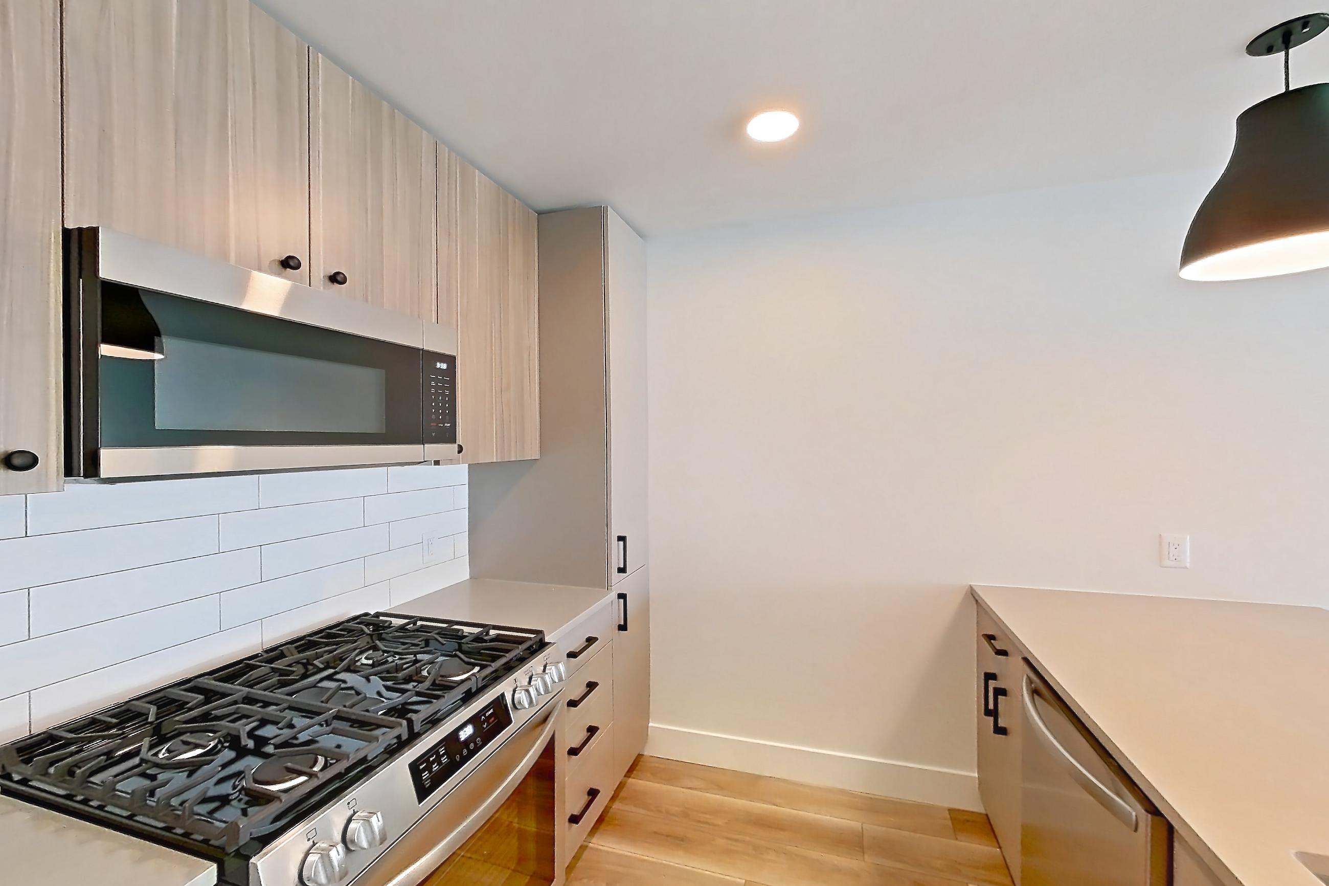 Kitchen with gas range, kitchen island, light countertops, light wood-finish flooring, oven/range, refrigerator, and stainless steel appliances, Apartment 711 at The Myles